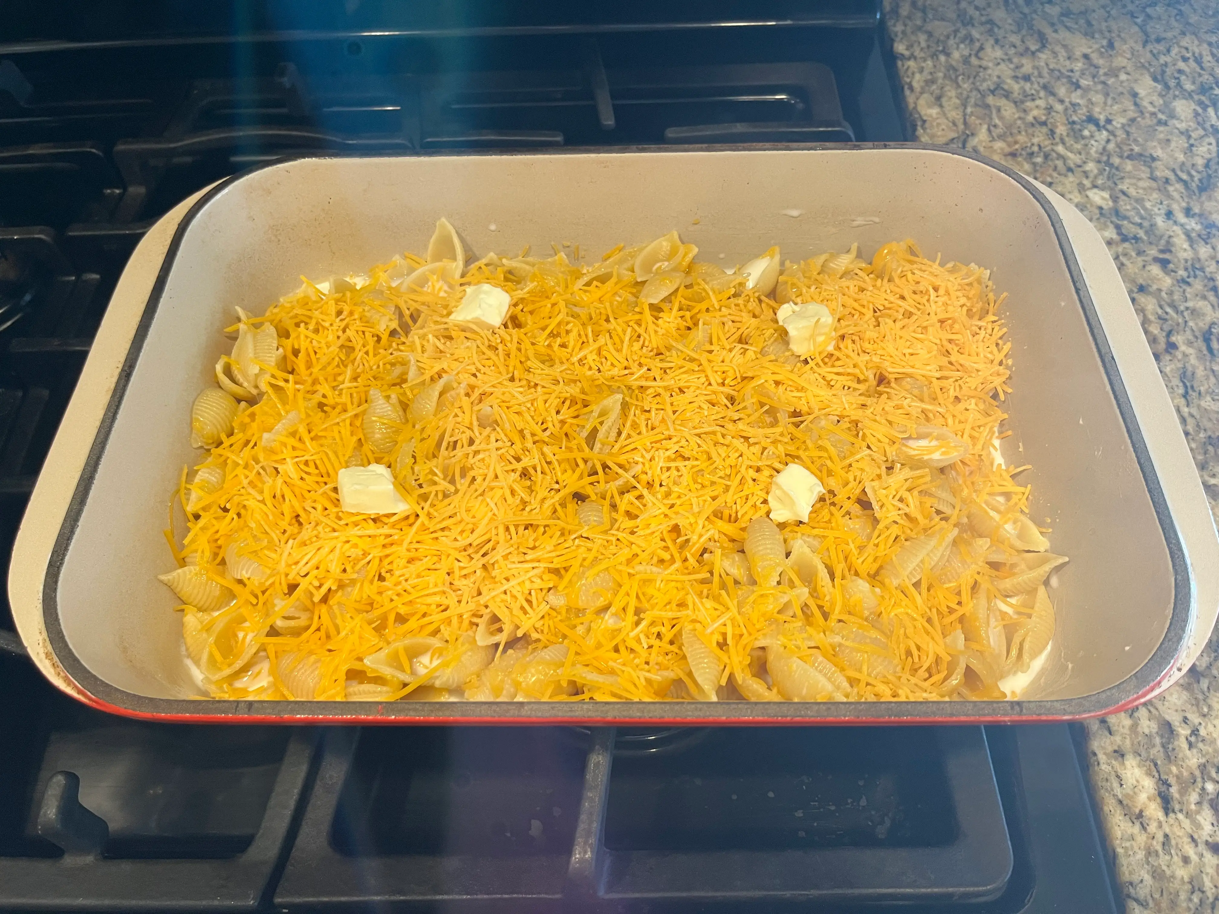 mac and cheese tray in oven with cheese and noodles inside and butter on top
