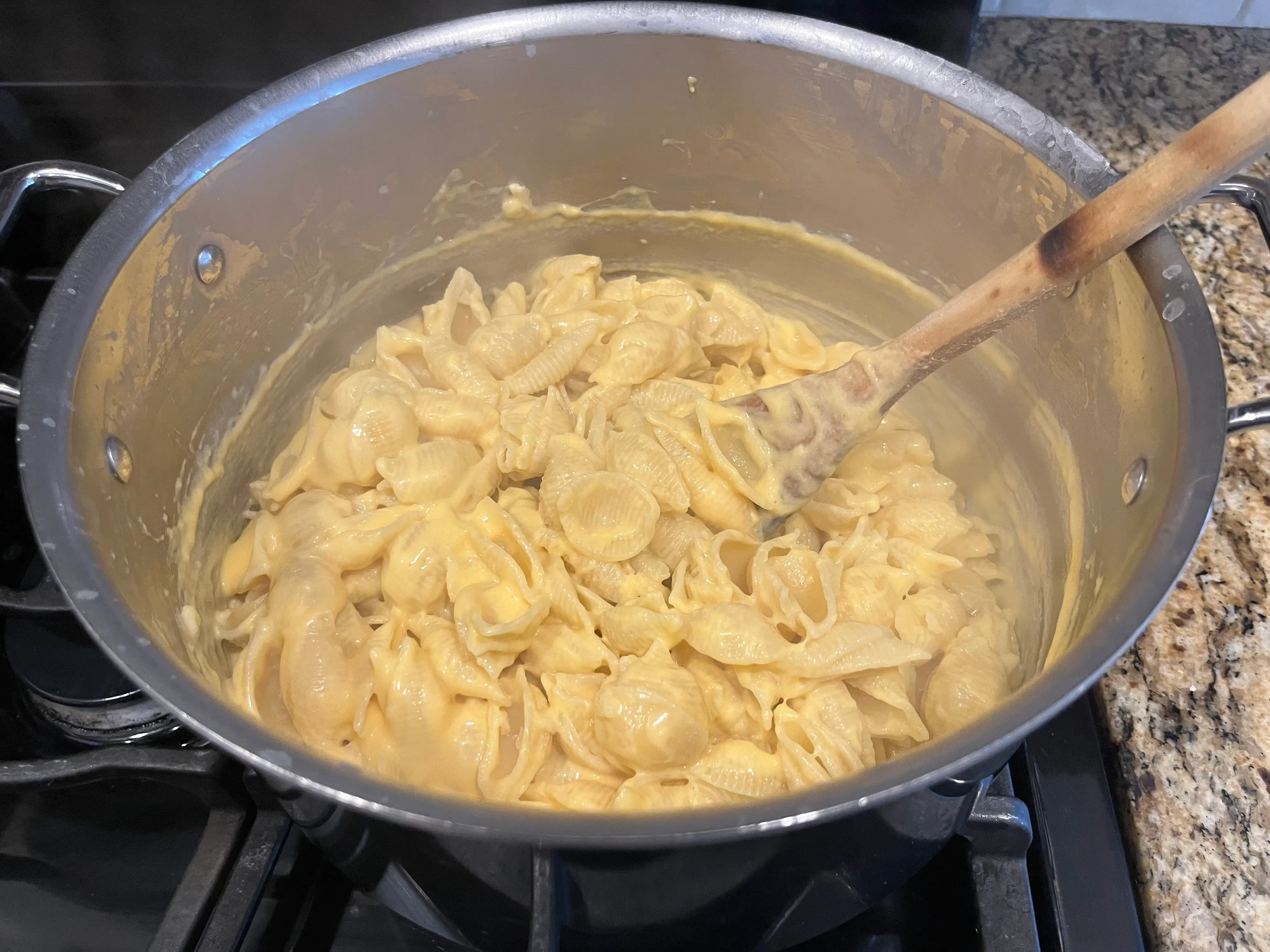 mac and cheese recipe in stove top with cheese and noodle mixed together and wooden spoon on right hand side