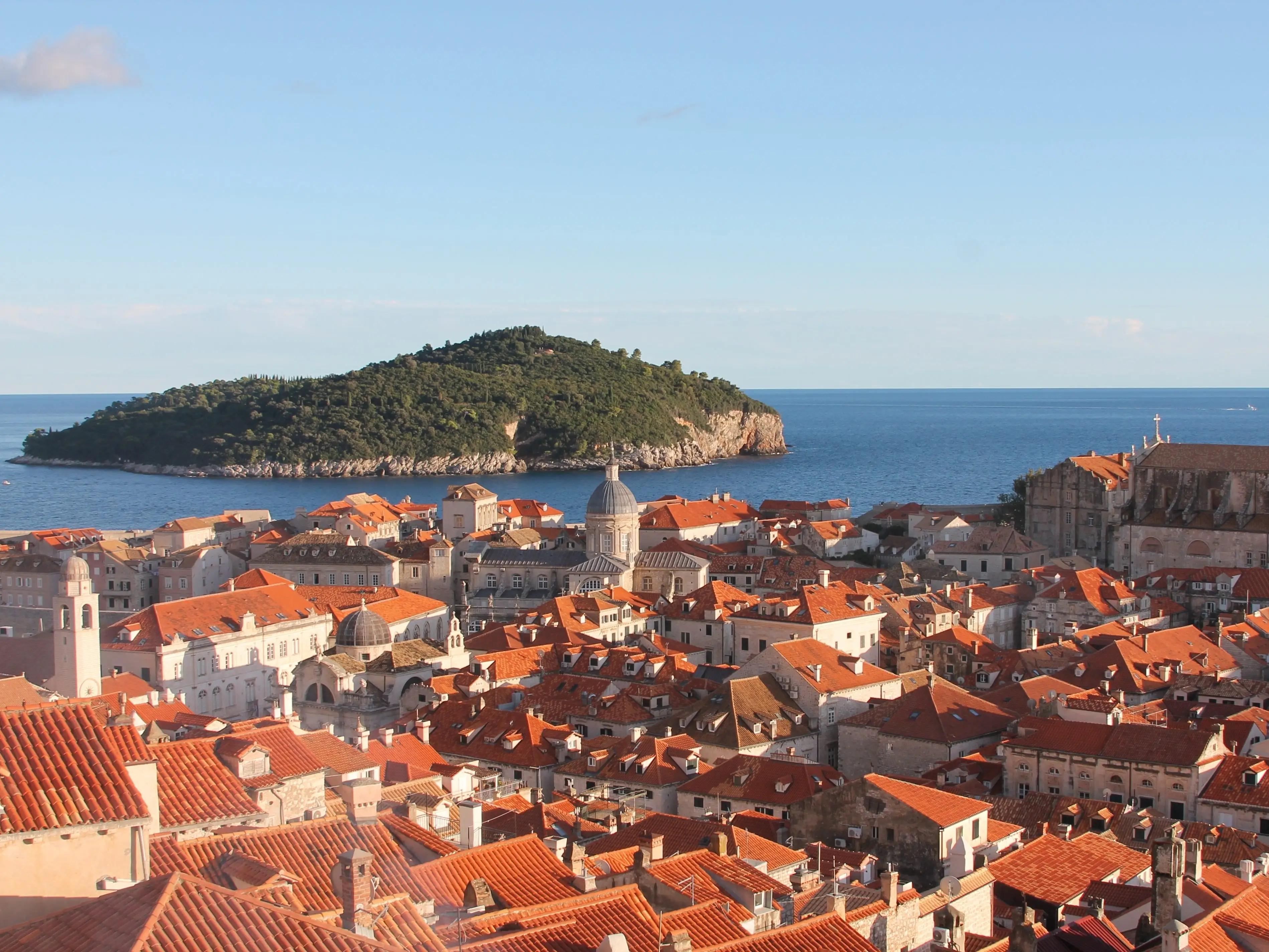 A wide shot overlooking Dubrovnik's old town with Lokrum Island in the distance.