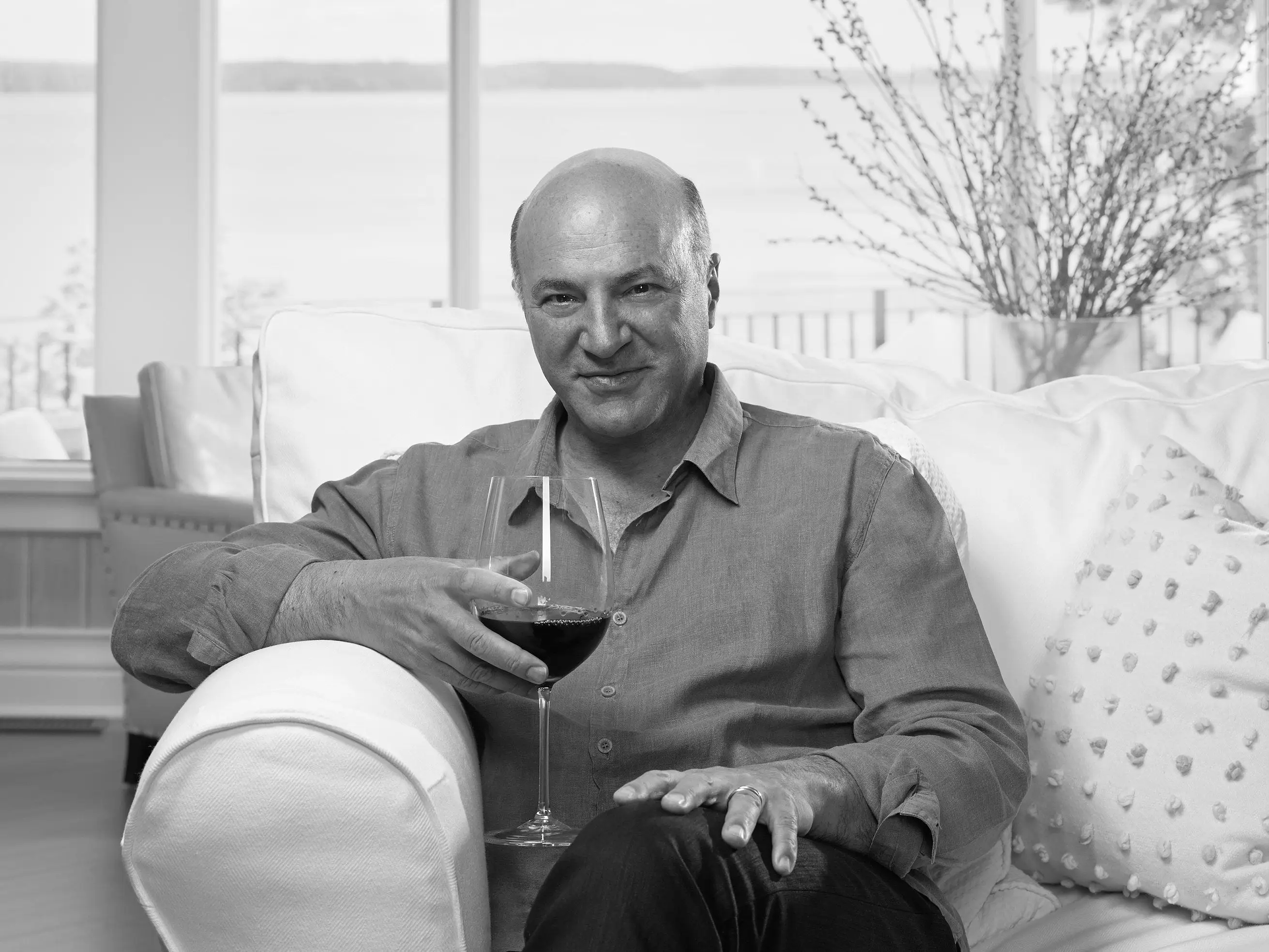 Kevin O'Leary sitting on a couch holding a glass of wine