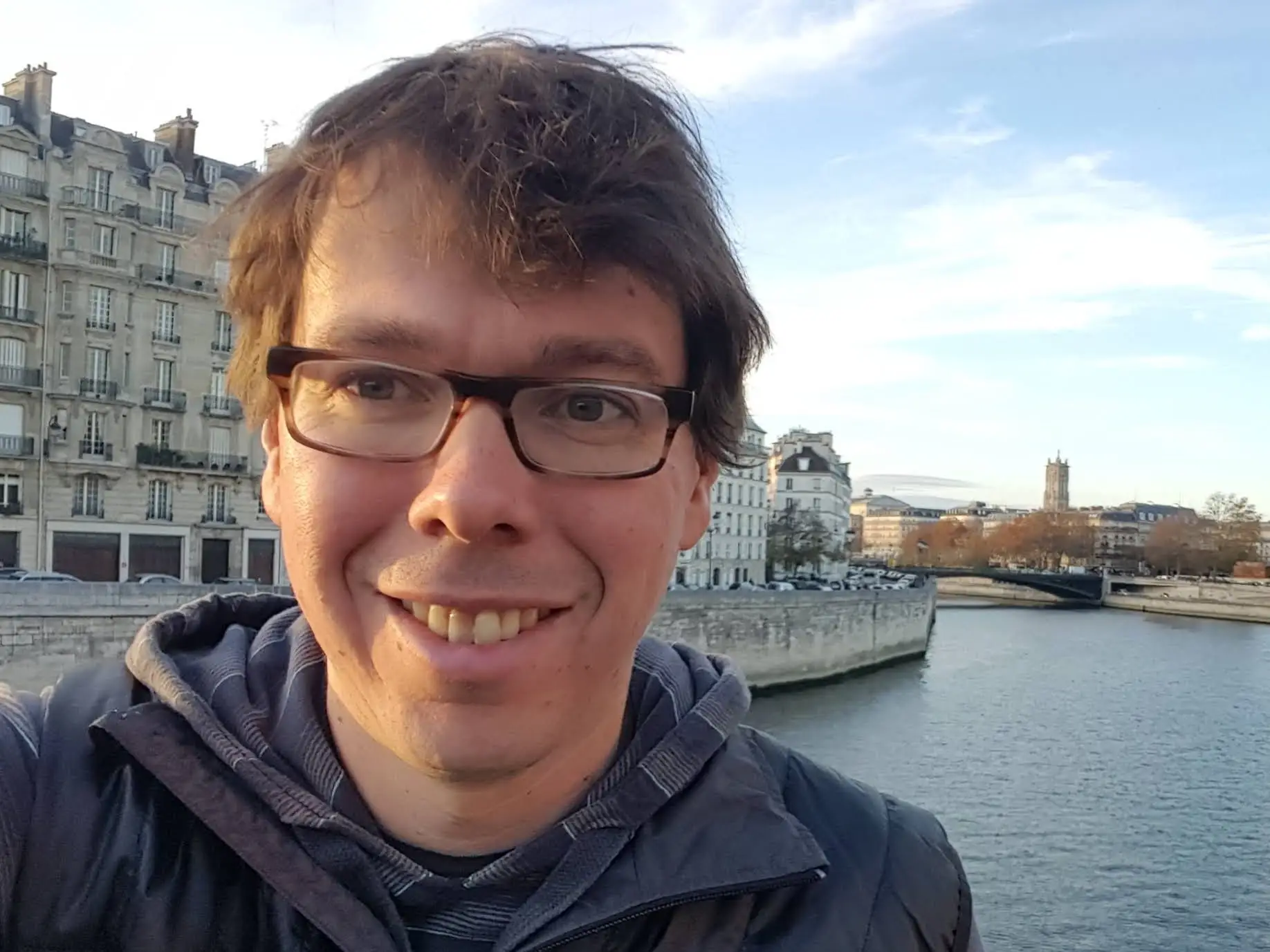 Judd Antin standing in front of a river. He's wearing a coat with the Airbnb logo.