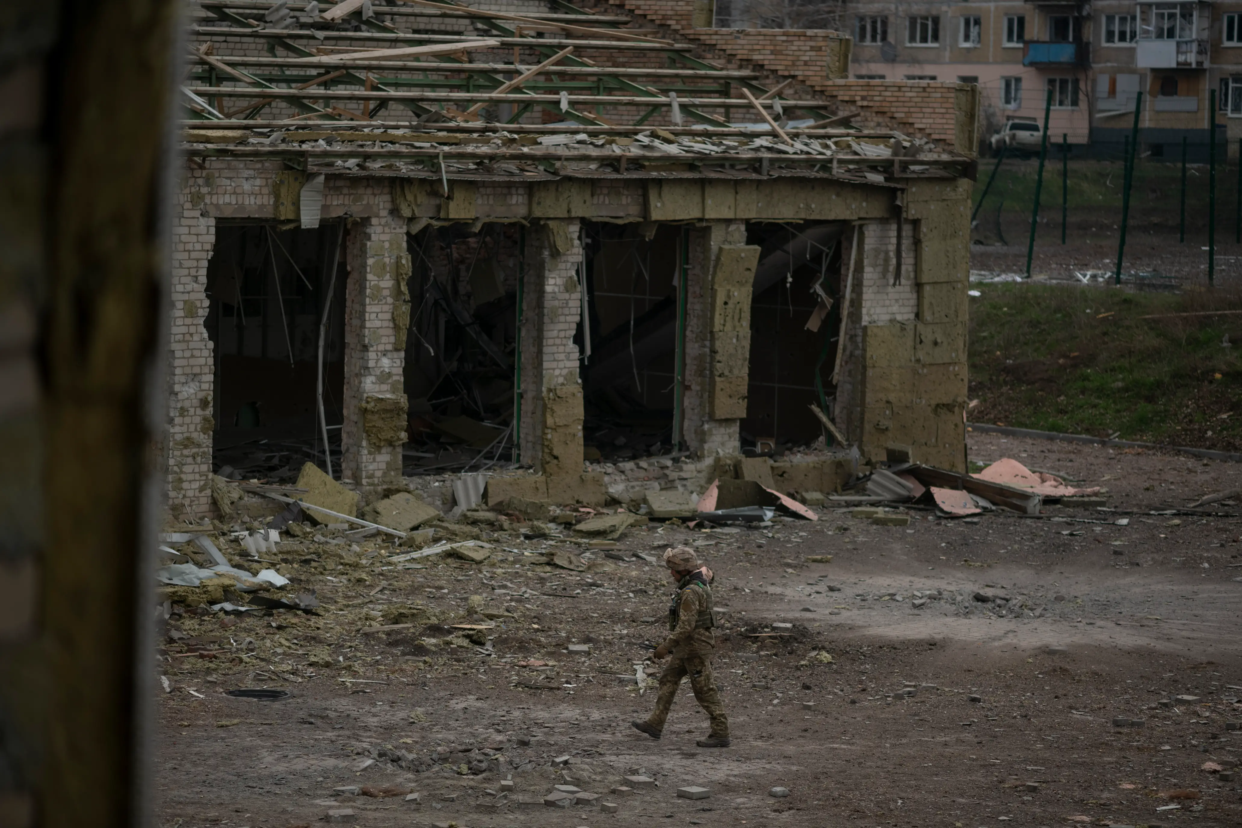A figure in khaki gear walks among destroyed buildings