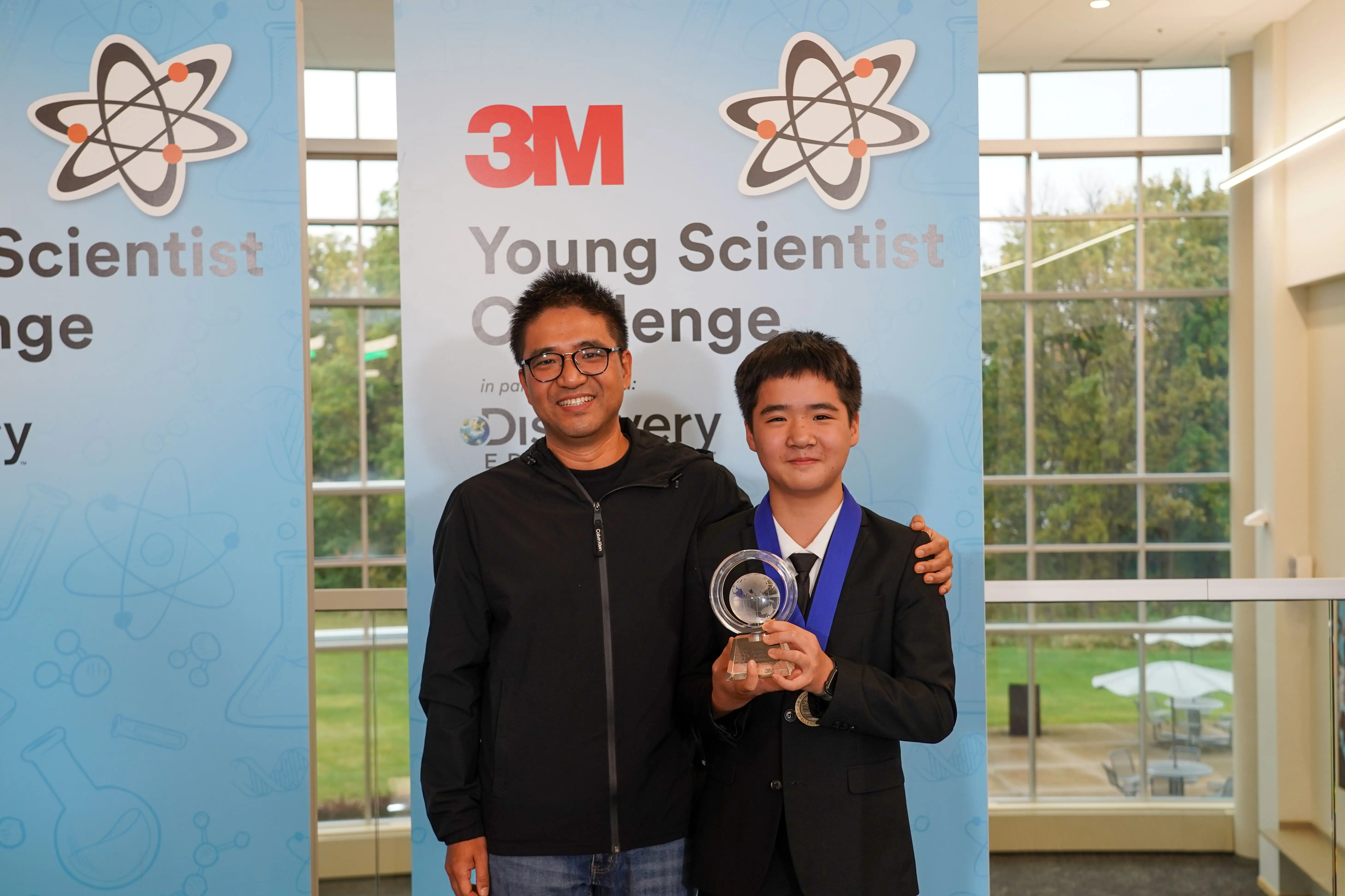 Kevin Tang with his father holding his first prize trophy for 3M Young Scientist Challenge