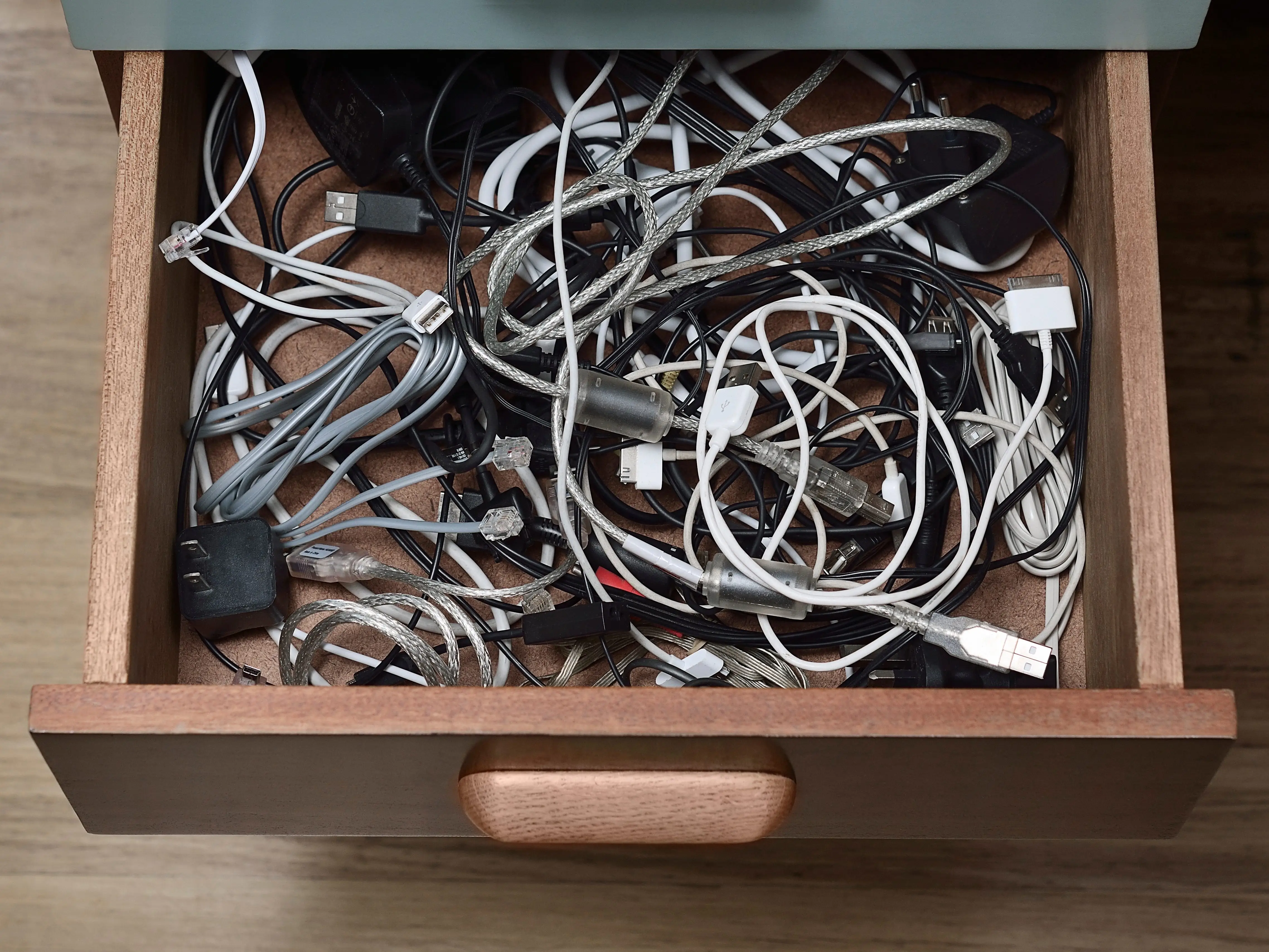 A desk drawer filled with cables, wires, and plugs.