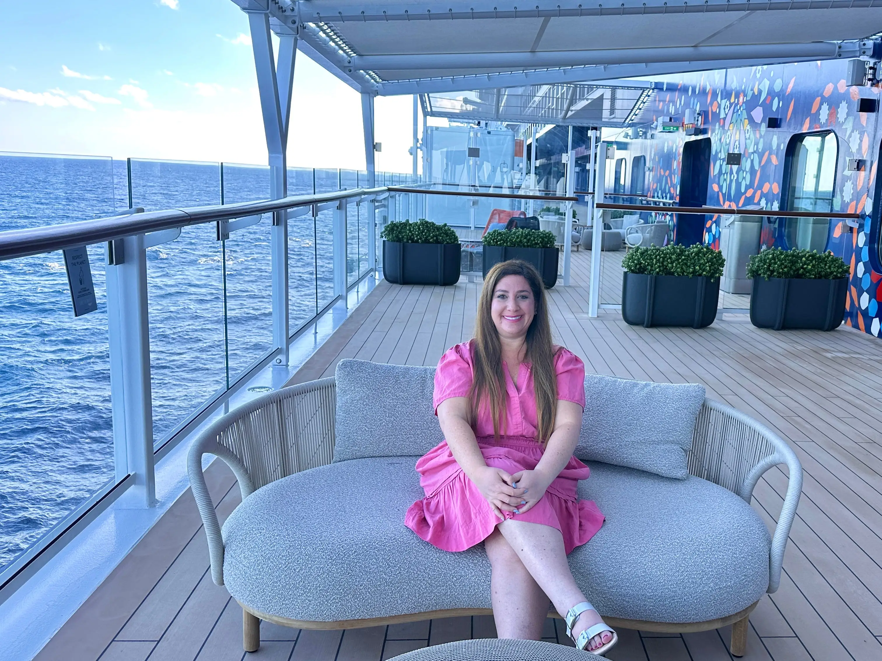 Author Jill Schildhouse smiling on bench outdoors on cruise ship deck of Celebrity Xcel