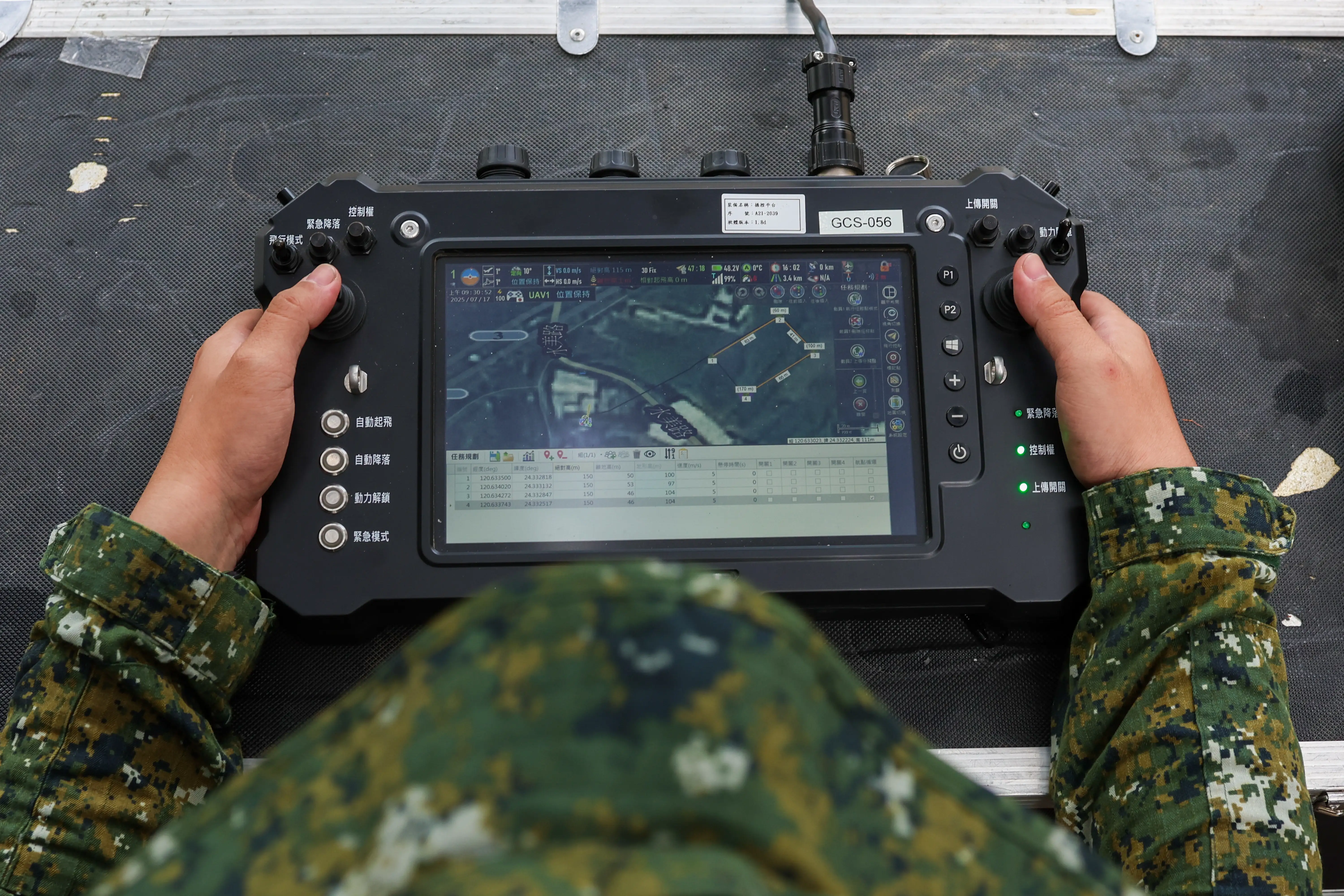 A man holds a large drone monitor with controls on either side of a large screen.