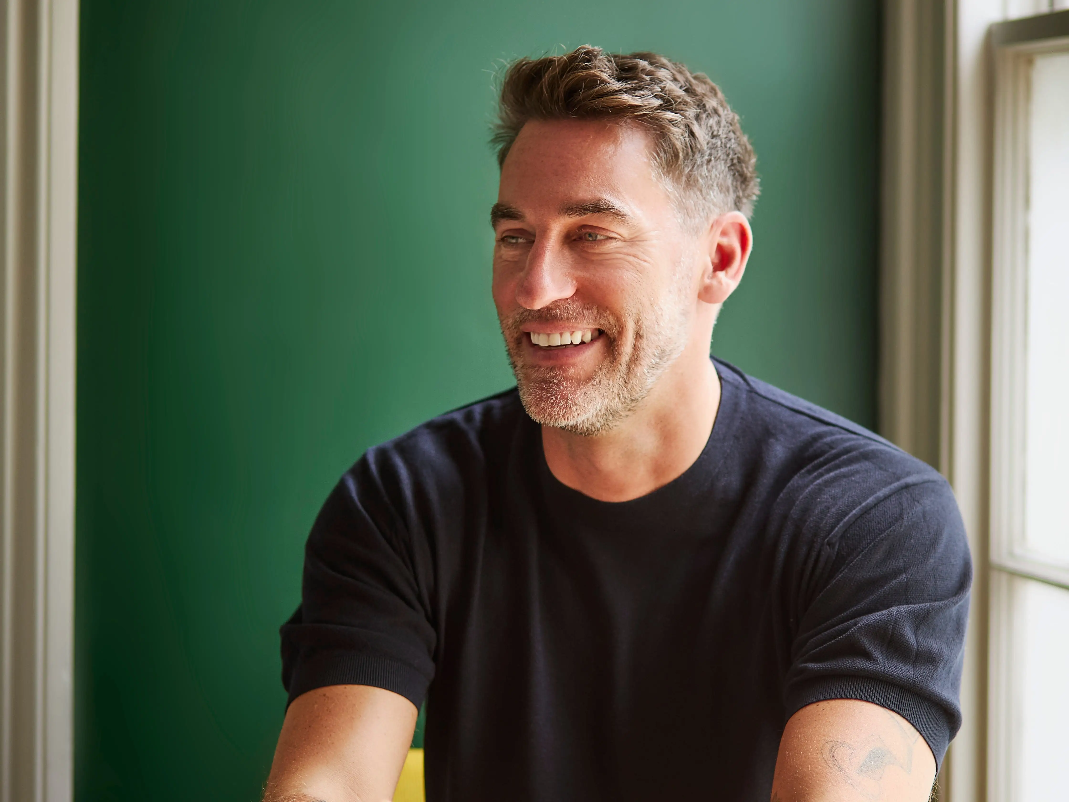 Rob Hobson sits at a table and smiles into the distance.