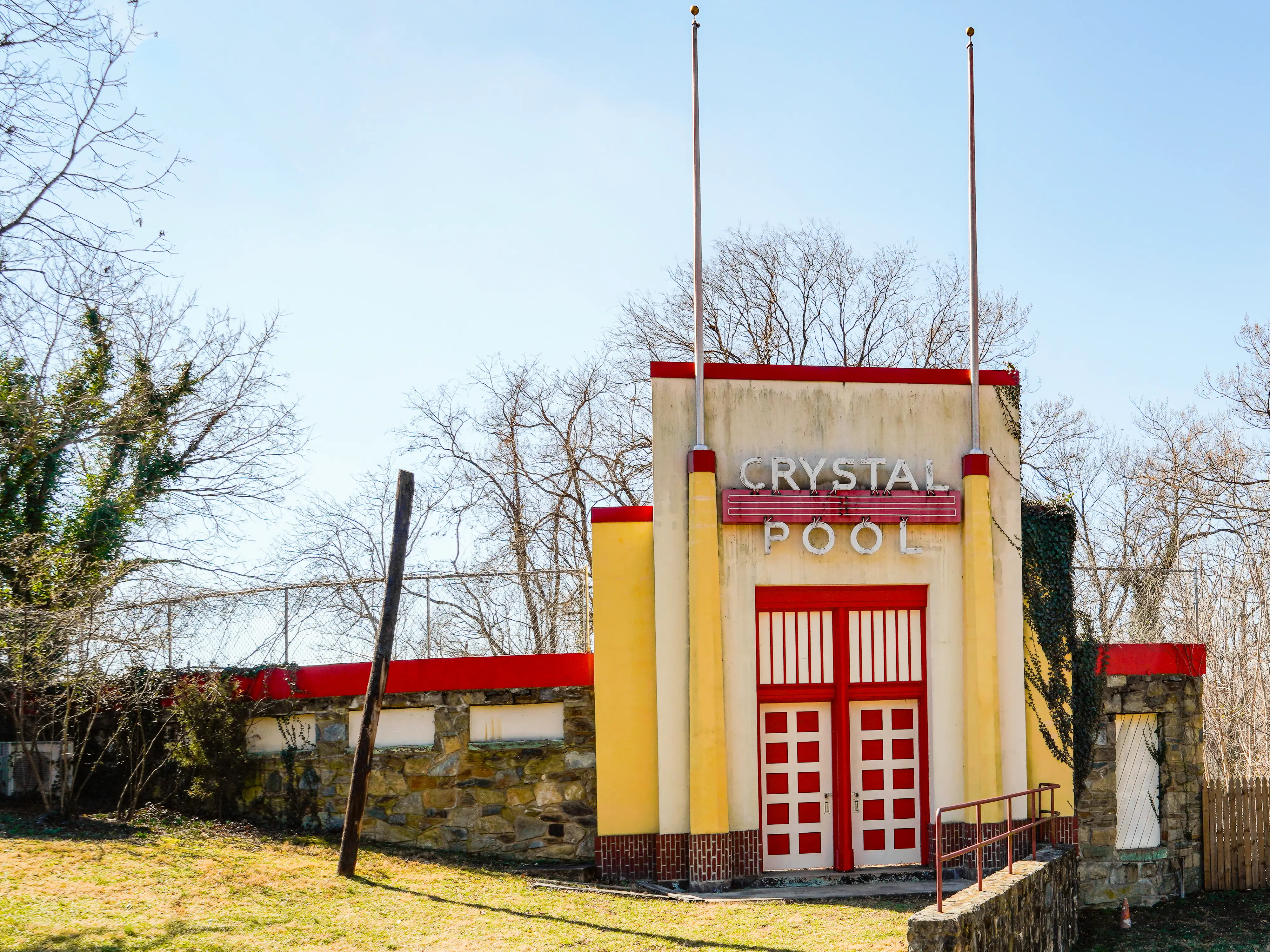 An abandoned Art Deco-style pool entrance with vines on the facade