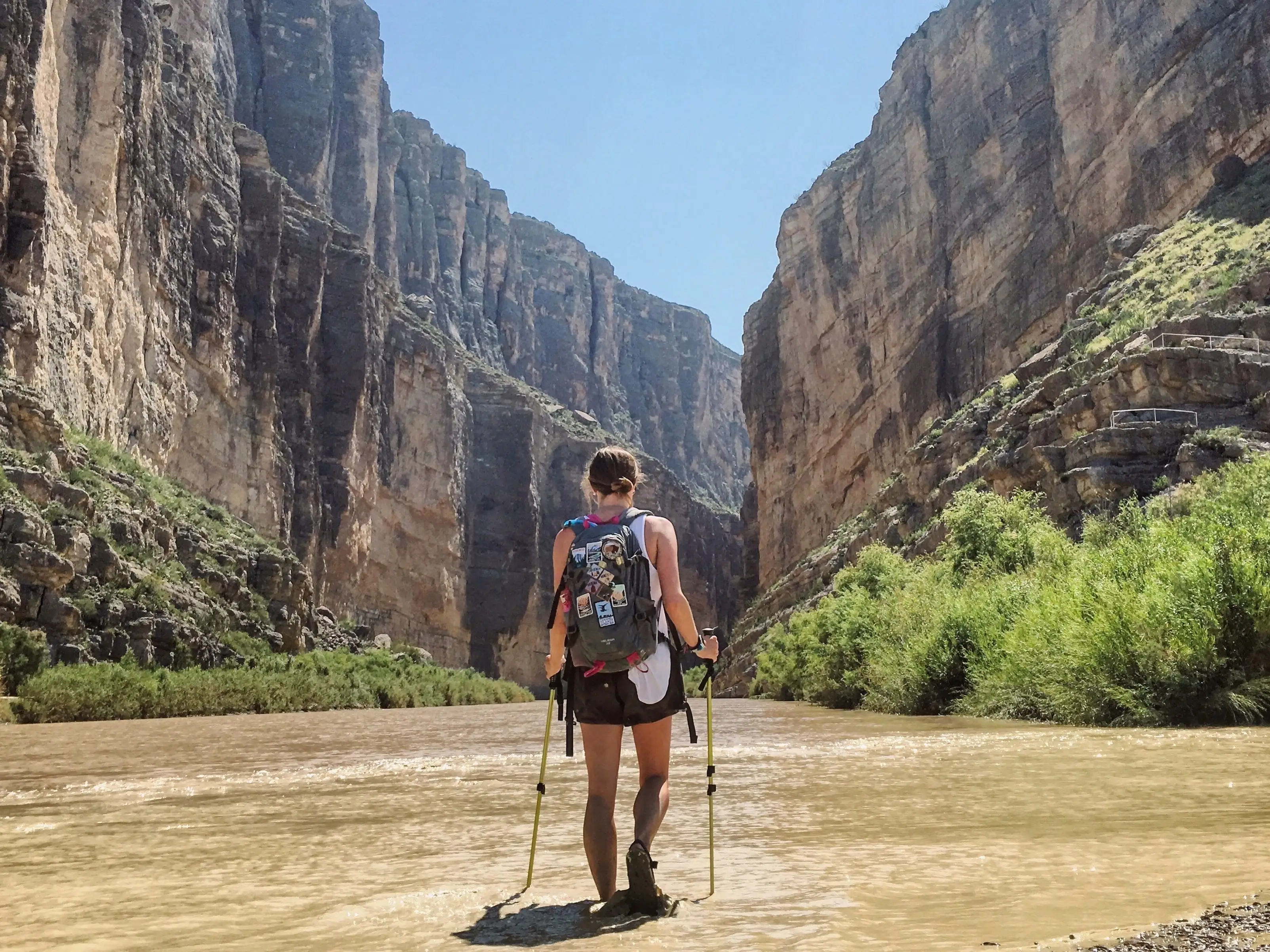 Emily uses walking sticks to hike in the water toward a large rock formation in Big Bend National Park.