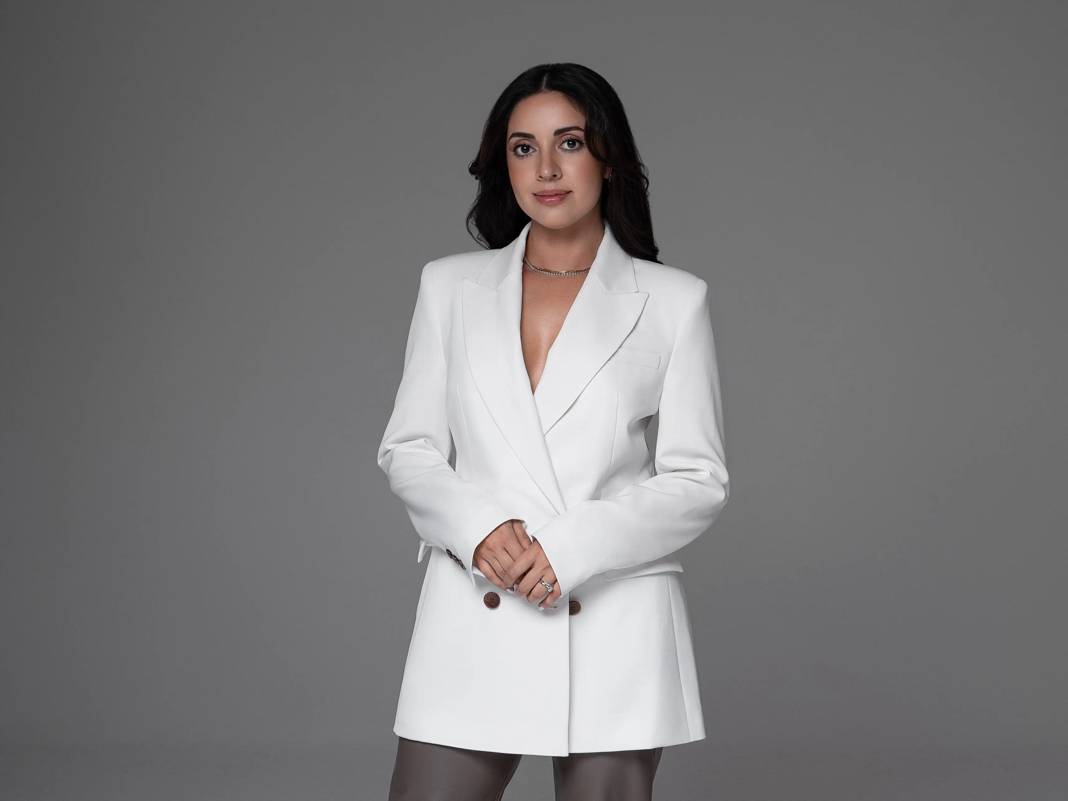 Headshot of a woman wearing a white blazer, black heels, and gray pants.