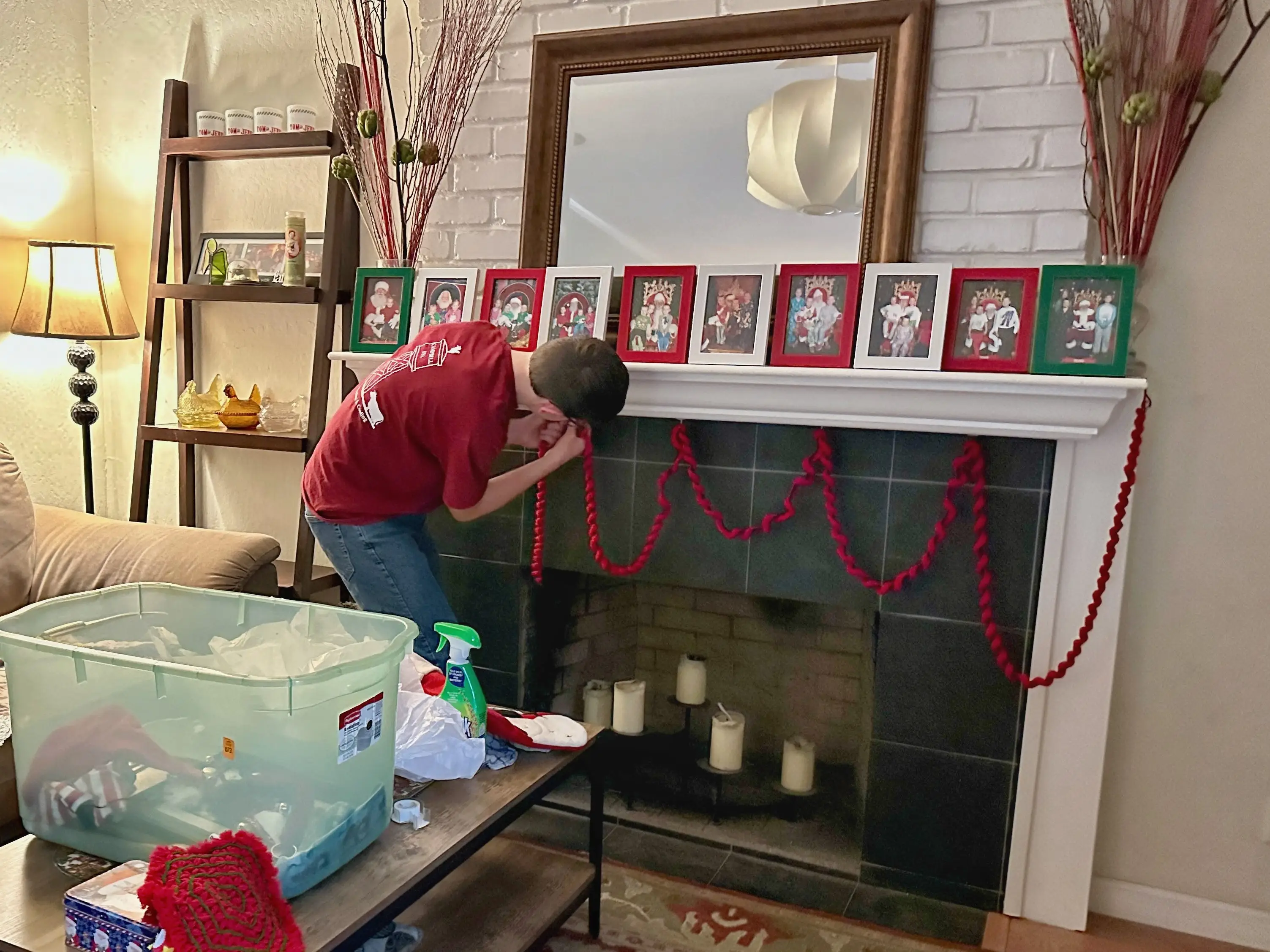 A teen boy hangs red garland on a mantle.