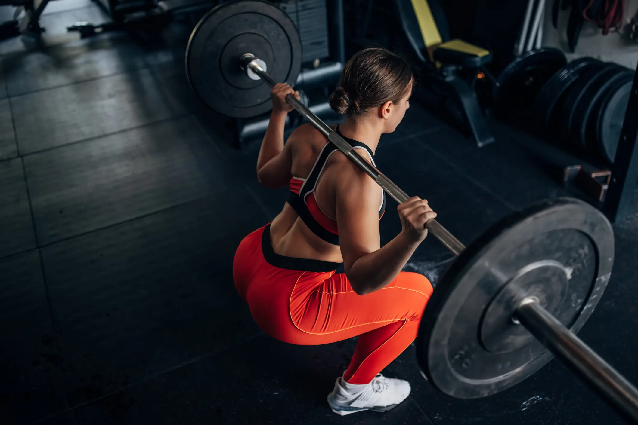 a woman performing a barbell back squat in the gym