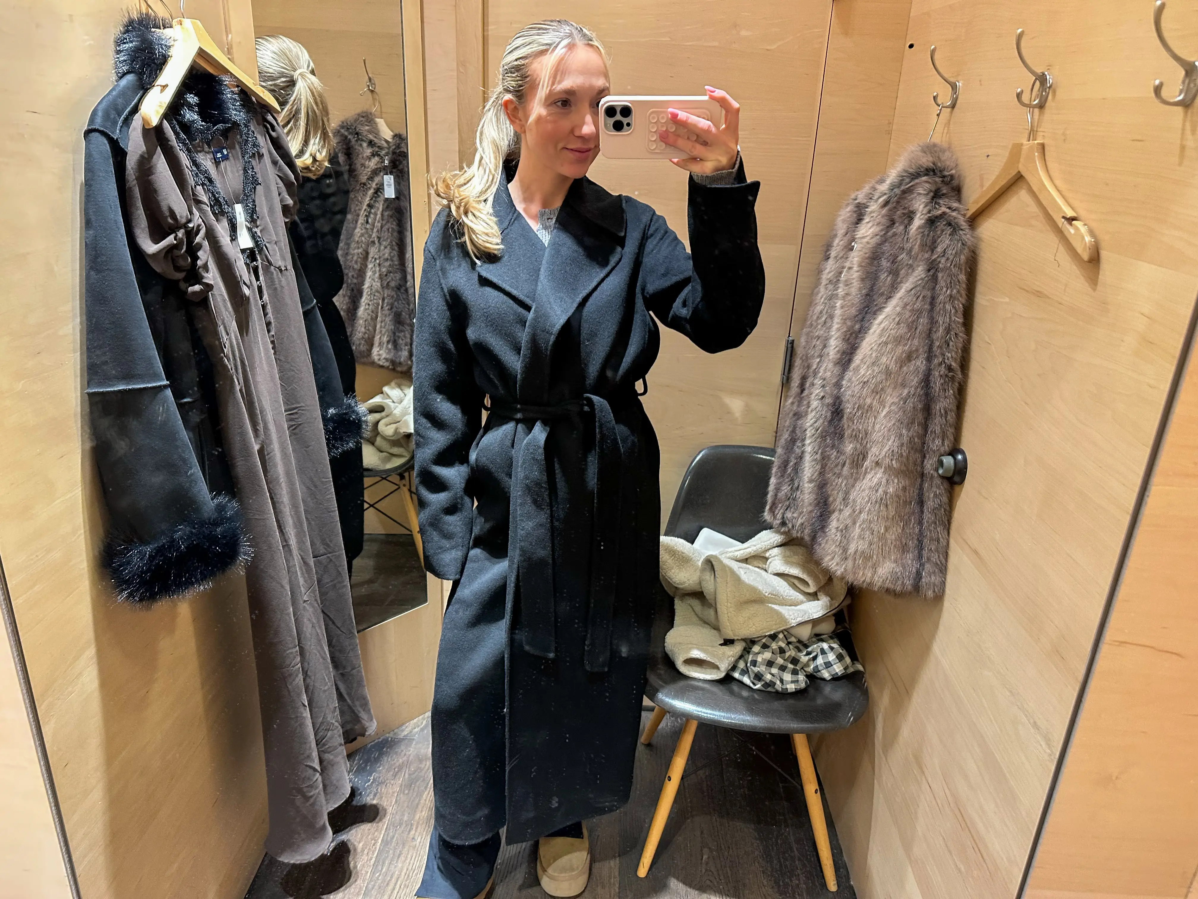 Chloe wears a long black peacoat in a fitting room.