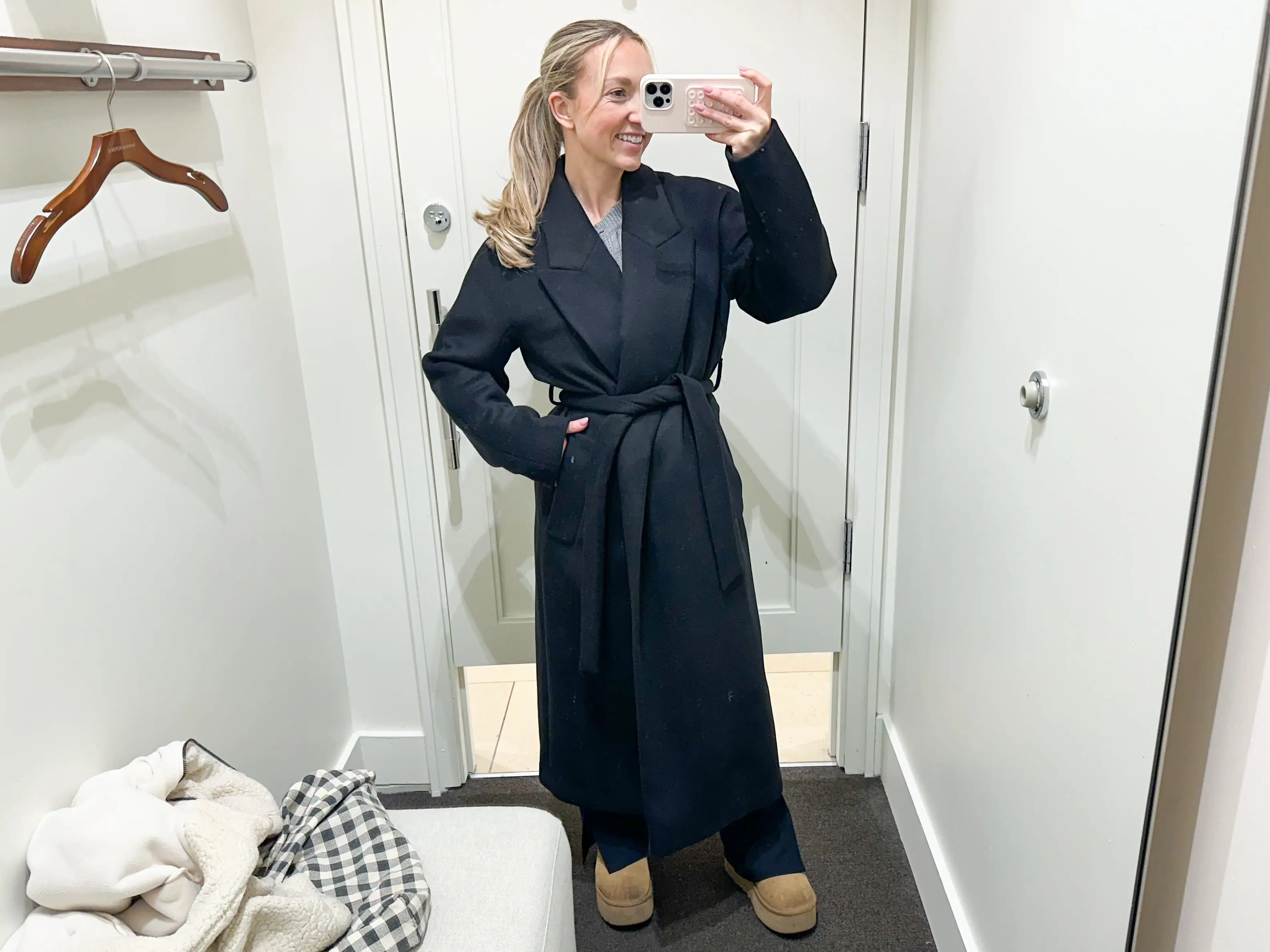 Chloe wears a long black peacoat in a fitting room.