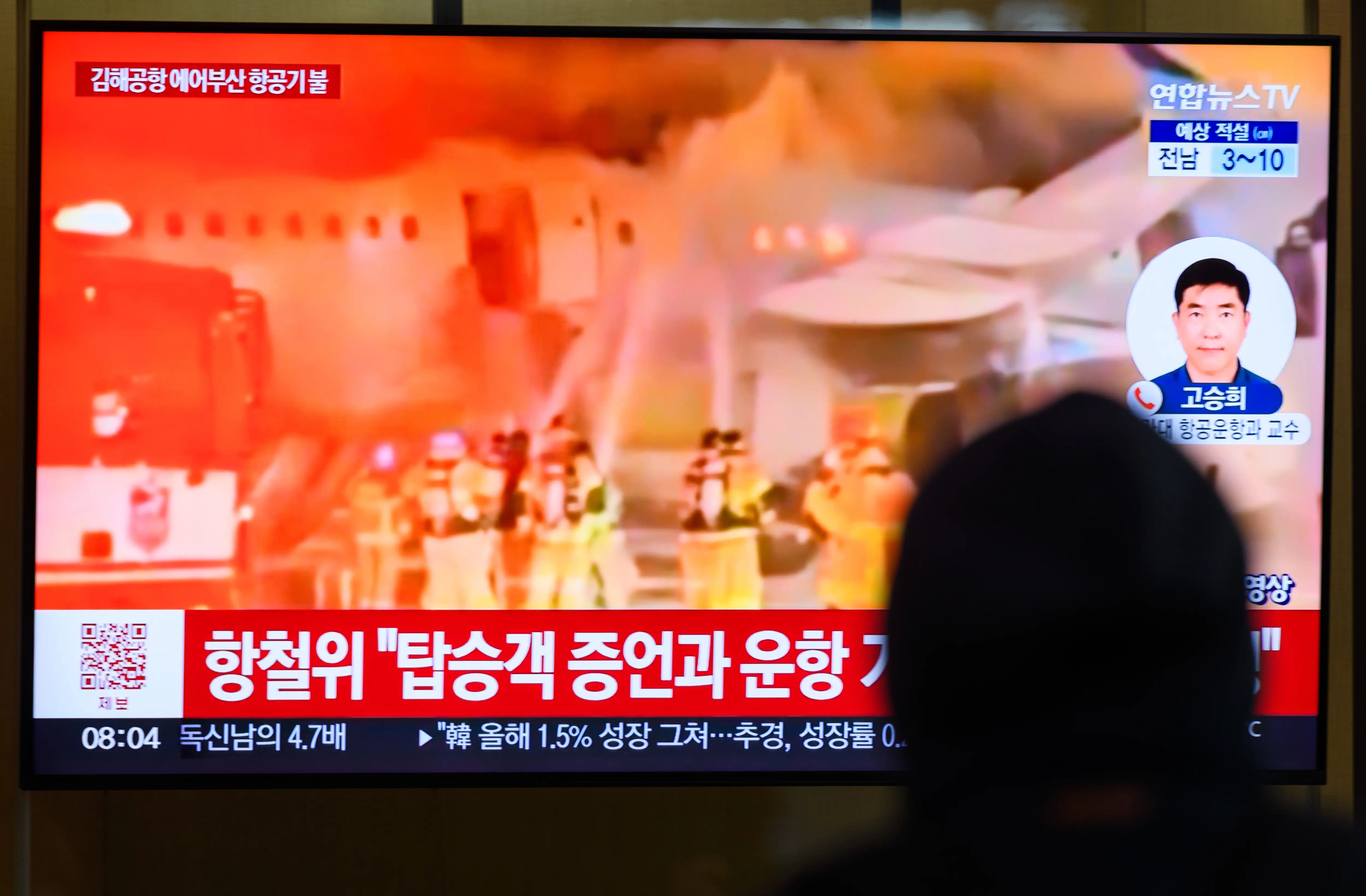 A person watches a 24-hour Yonhap news TV broadcast at Seoul Railway Station showed a news broadcast with an Air Busan airplane on fire at Gimhae International Airport in Busan.