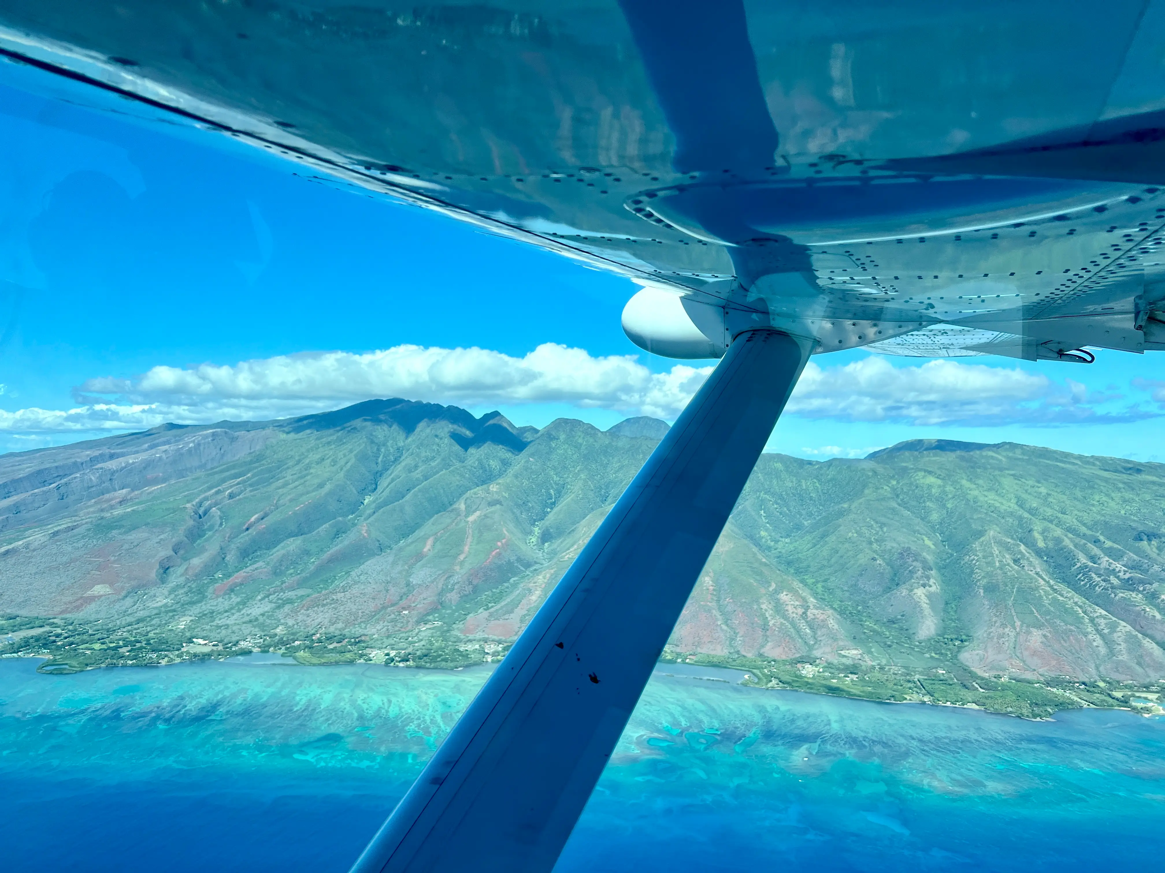 View under propellor outside plane window of mountains, blue water