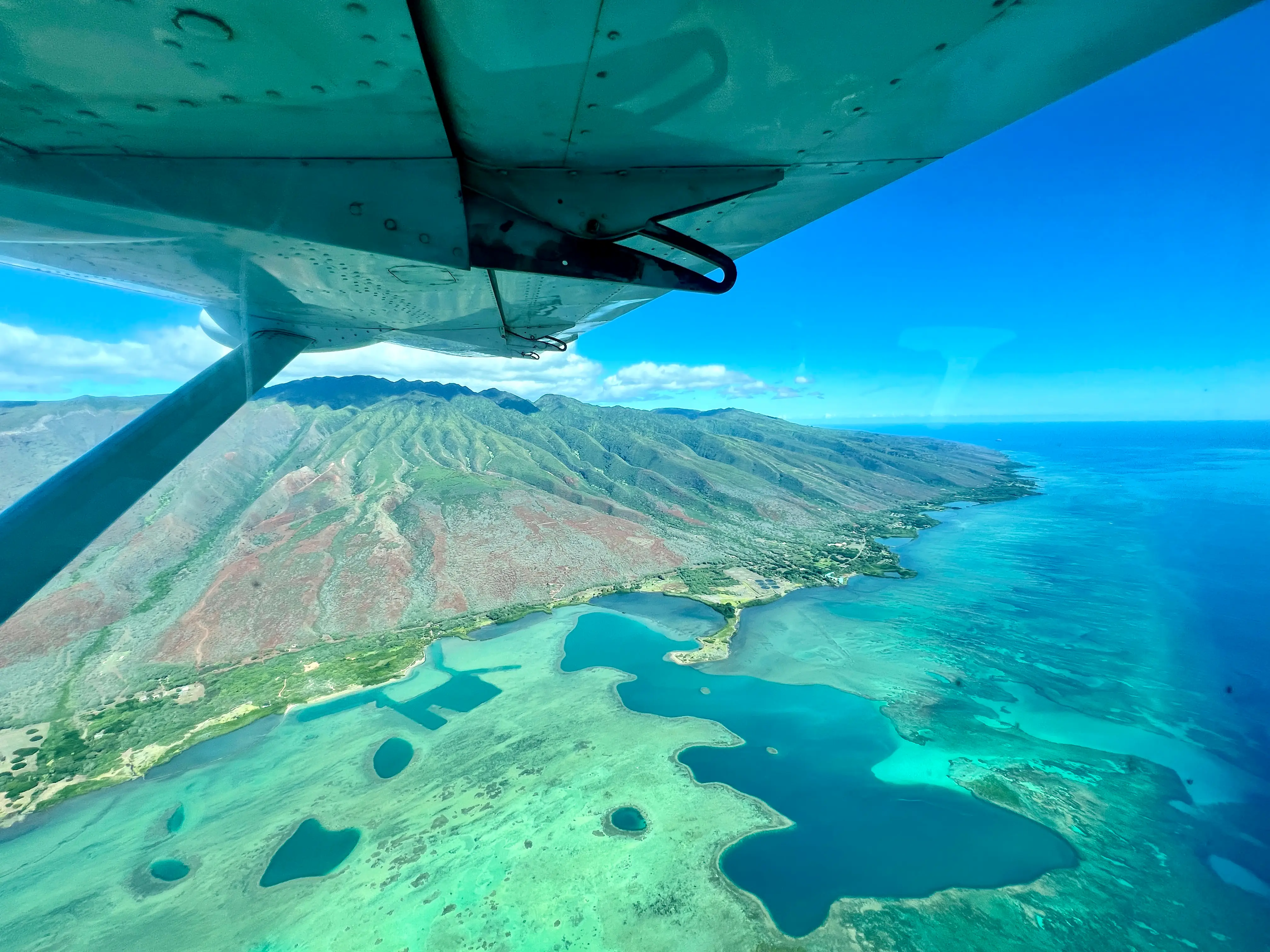 View of blue water, mountains below plane wing from window