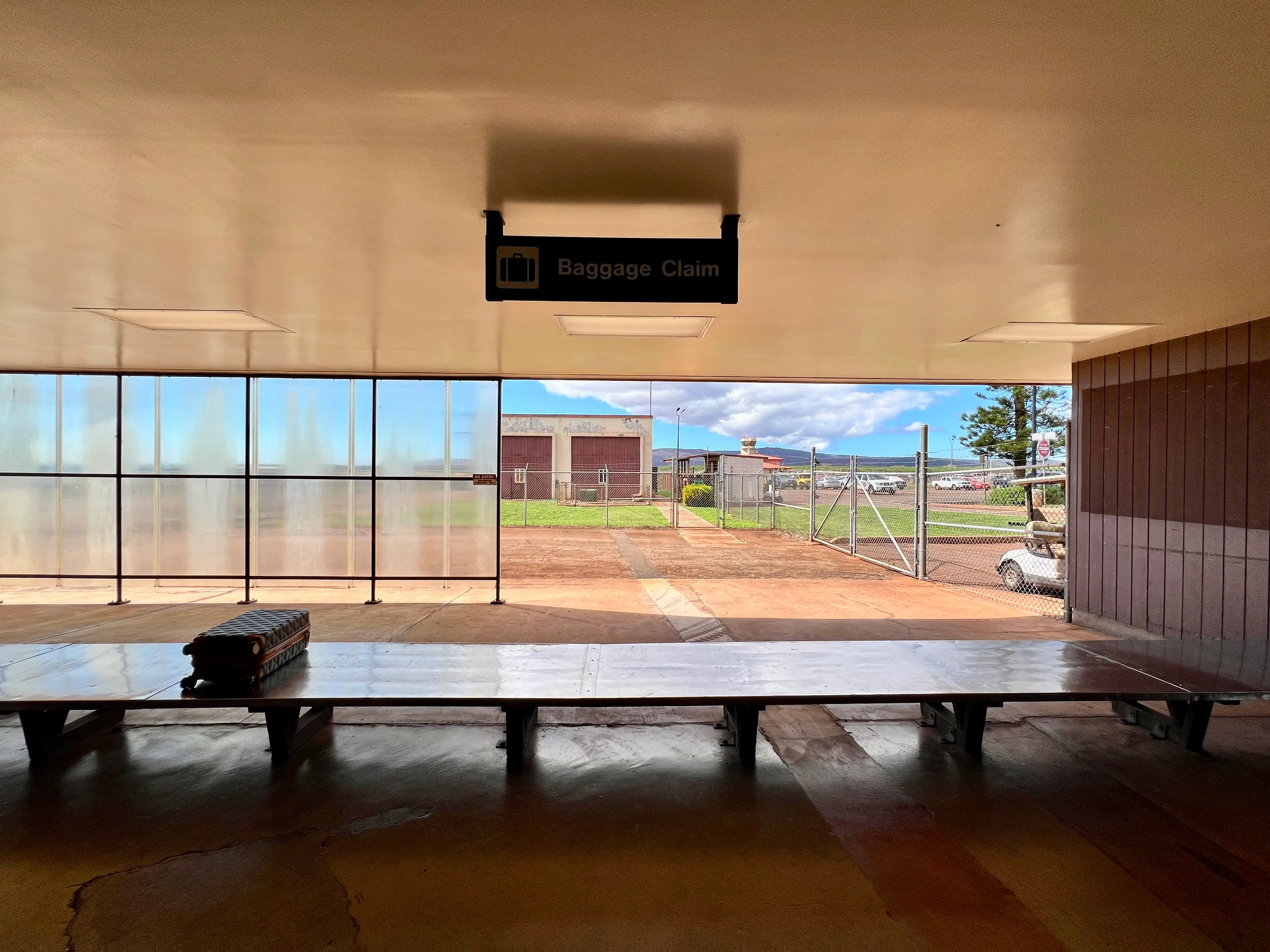 Baggage claim in airport with large wood table with one suitcase on it and open-air windows