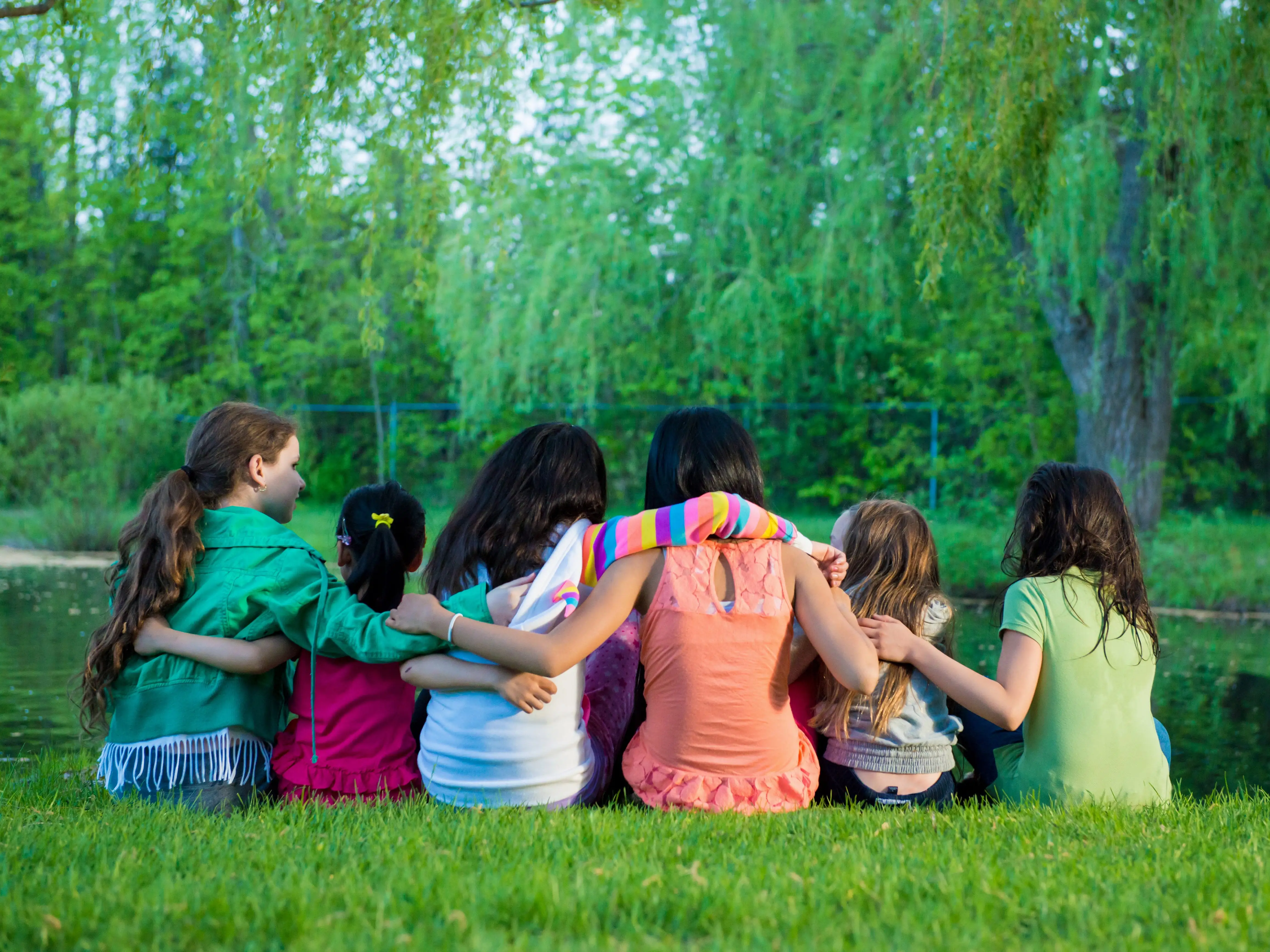 Six kids sitting on a lawn embracing.