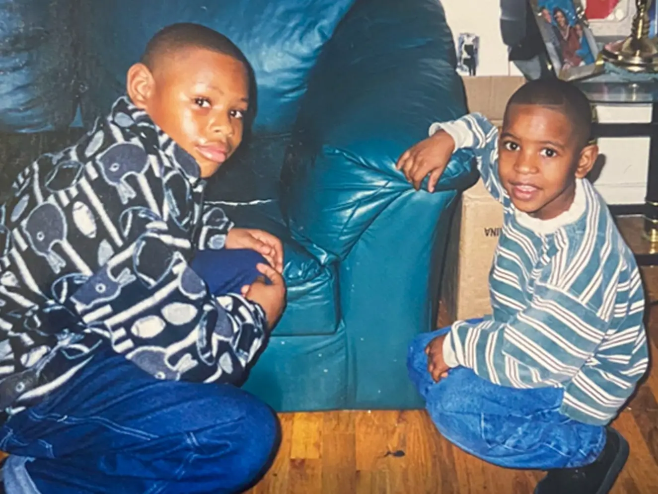 Two young boys are sitting beside a sofa.