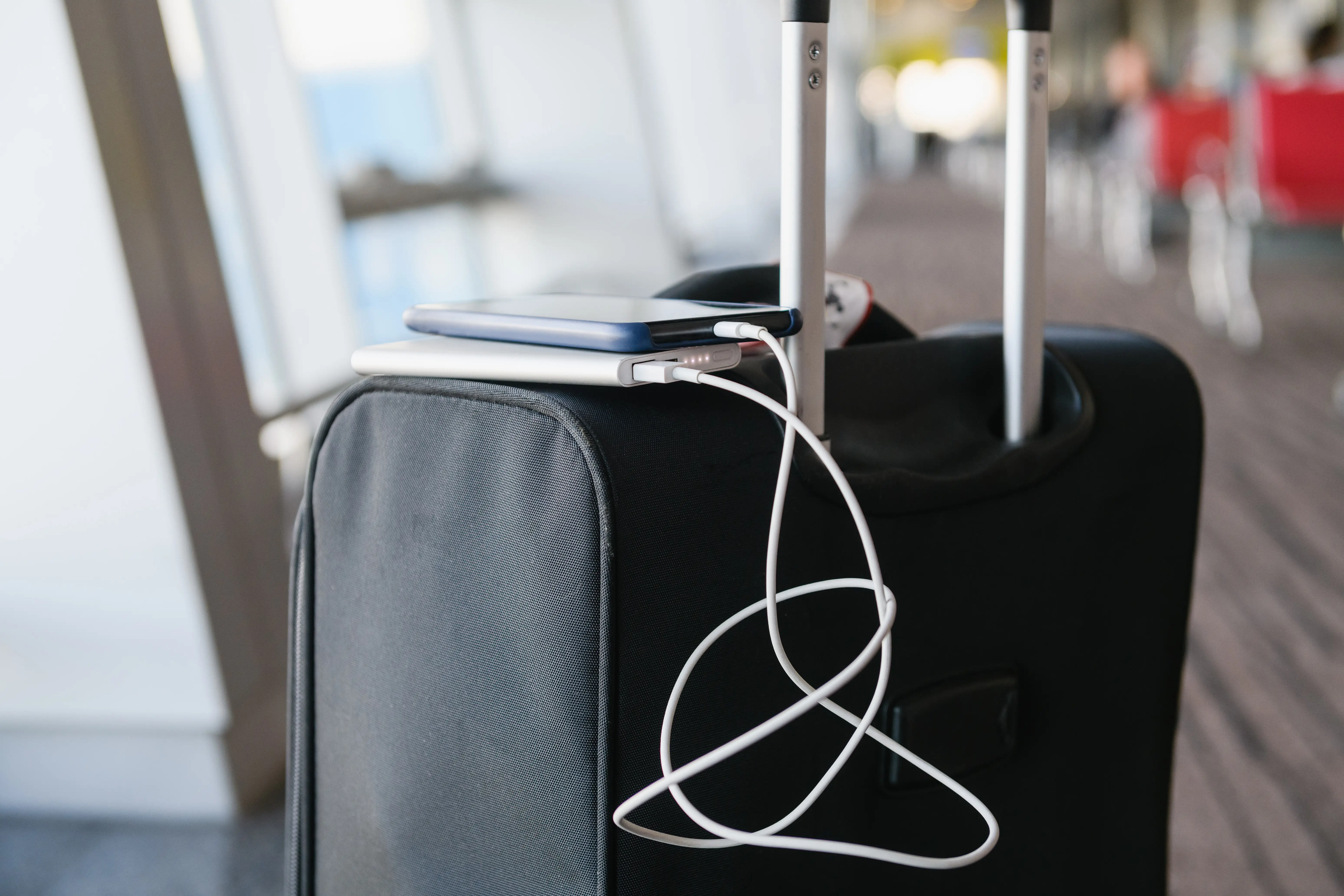 A power bank chargers a phone on top of a suitcase.
