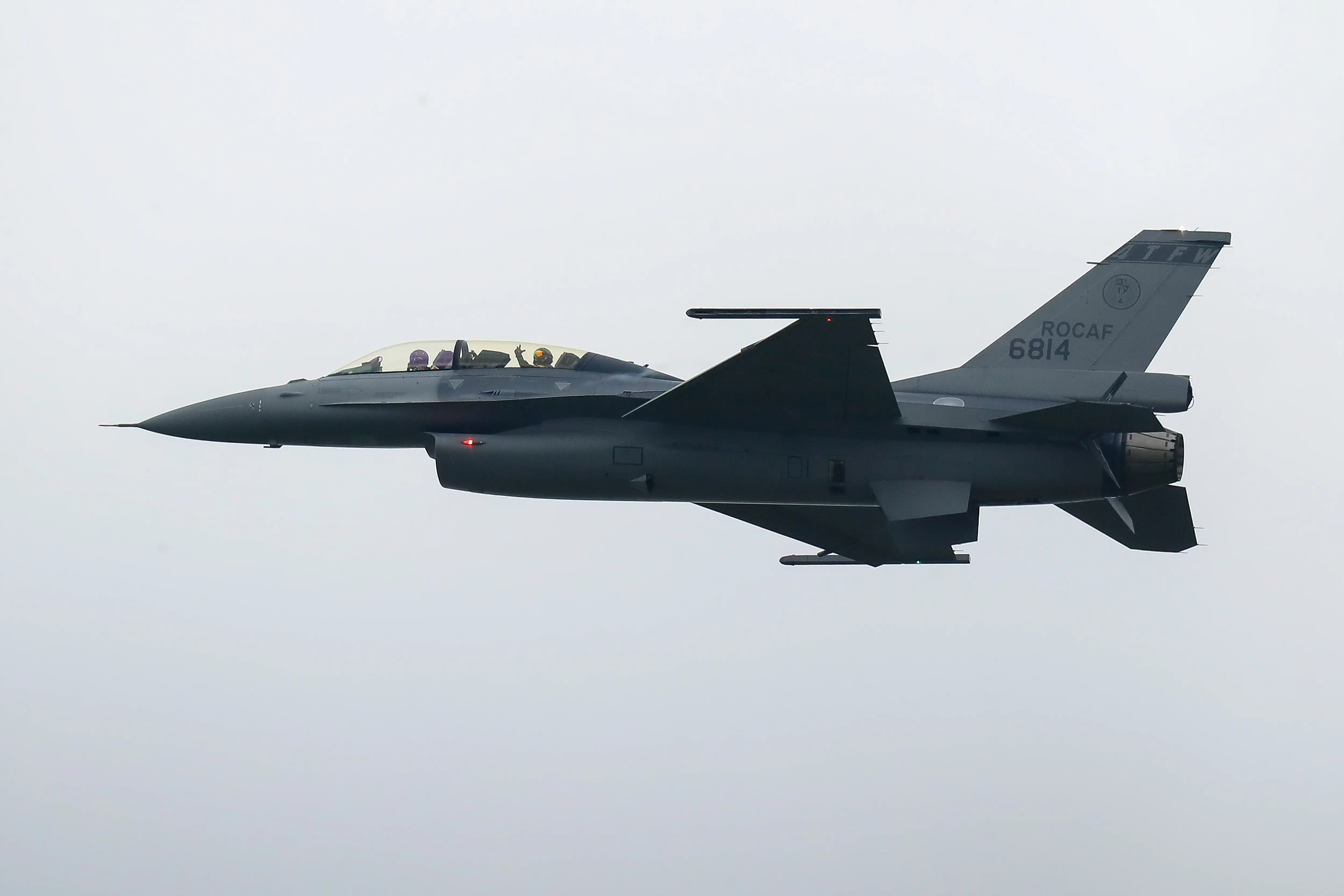 The side view of an F-16 is seen as it flies against a grey sky.