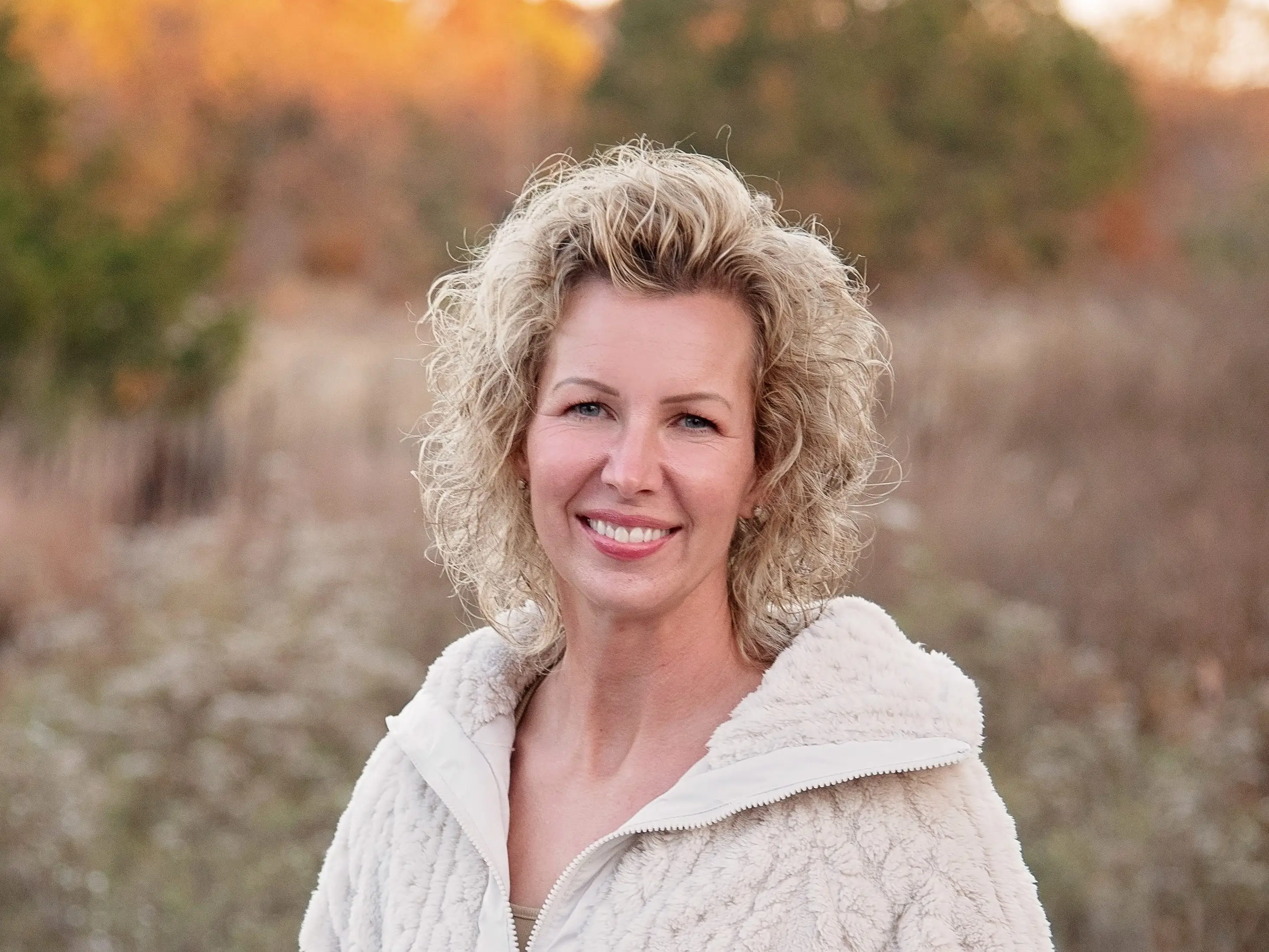 Tiffany Haynes wearing a white zip-up sweater and standing in a field.