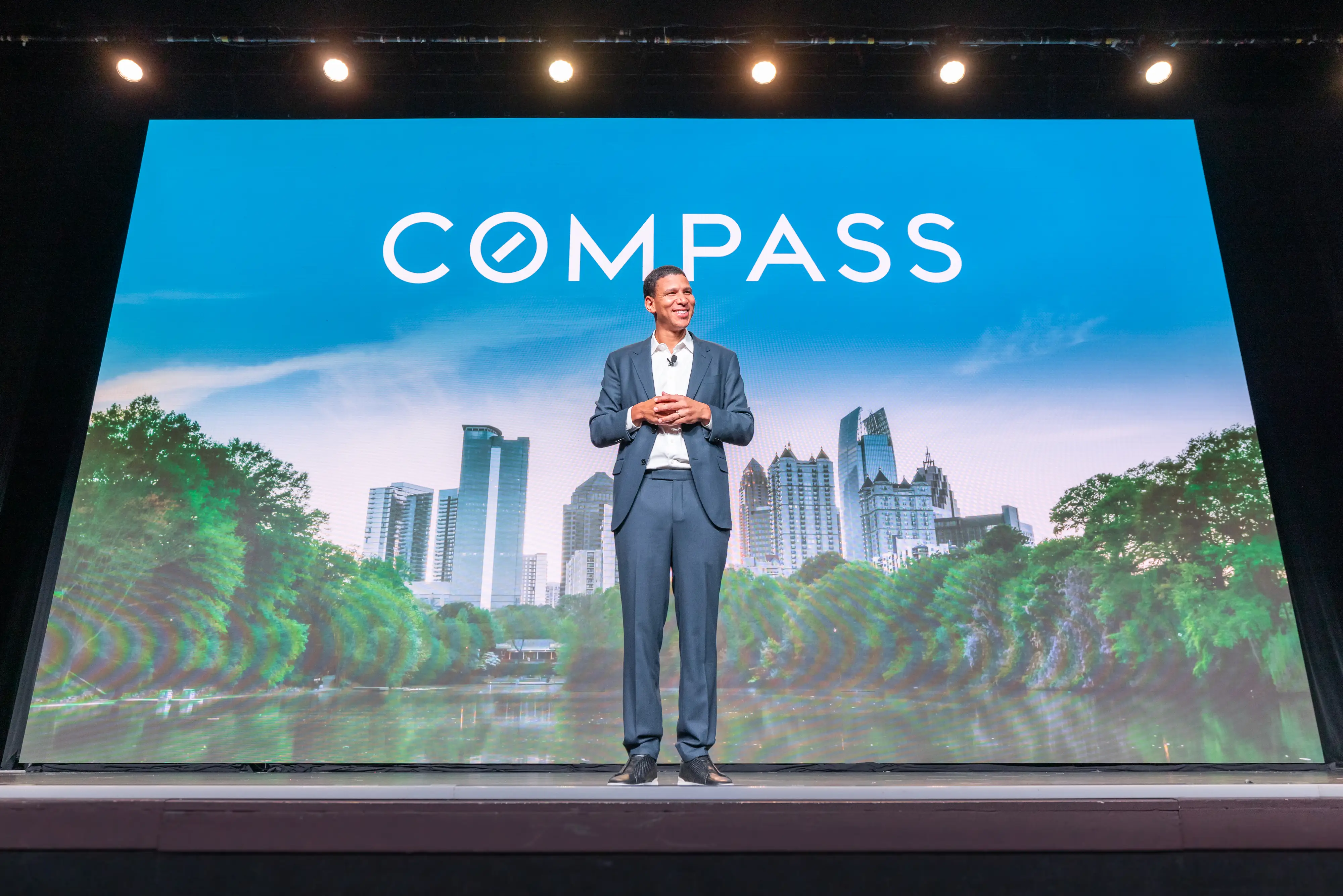 Compass CEO Robert Reffkin, dressed in a suit, stands smiling onstage at a company retreat in Atlanta