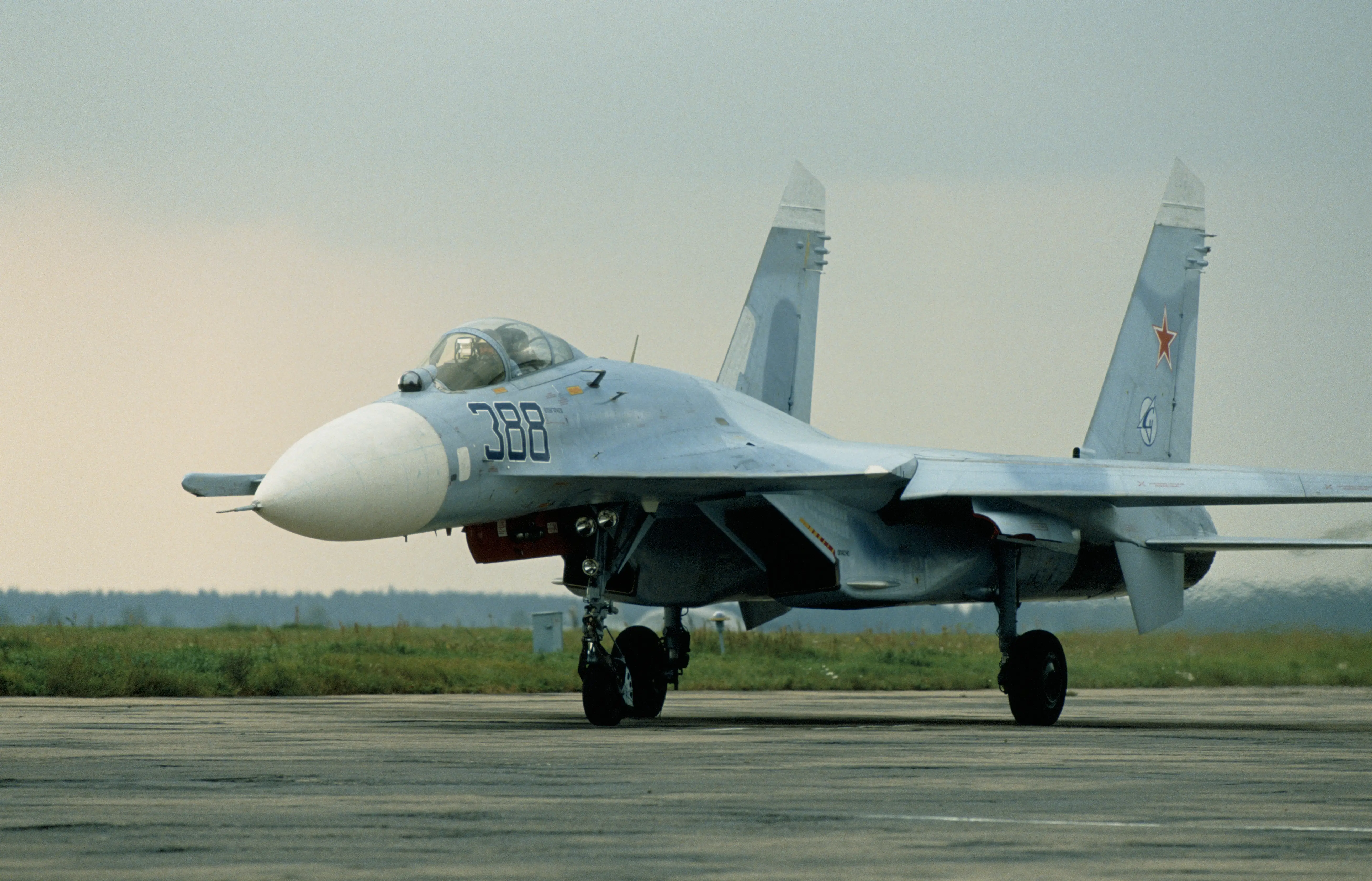 A grey fighter jet on a runway with a grey sky behind