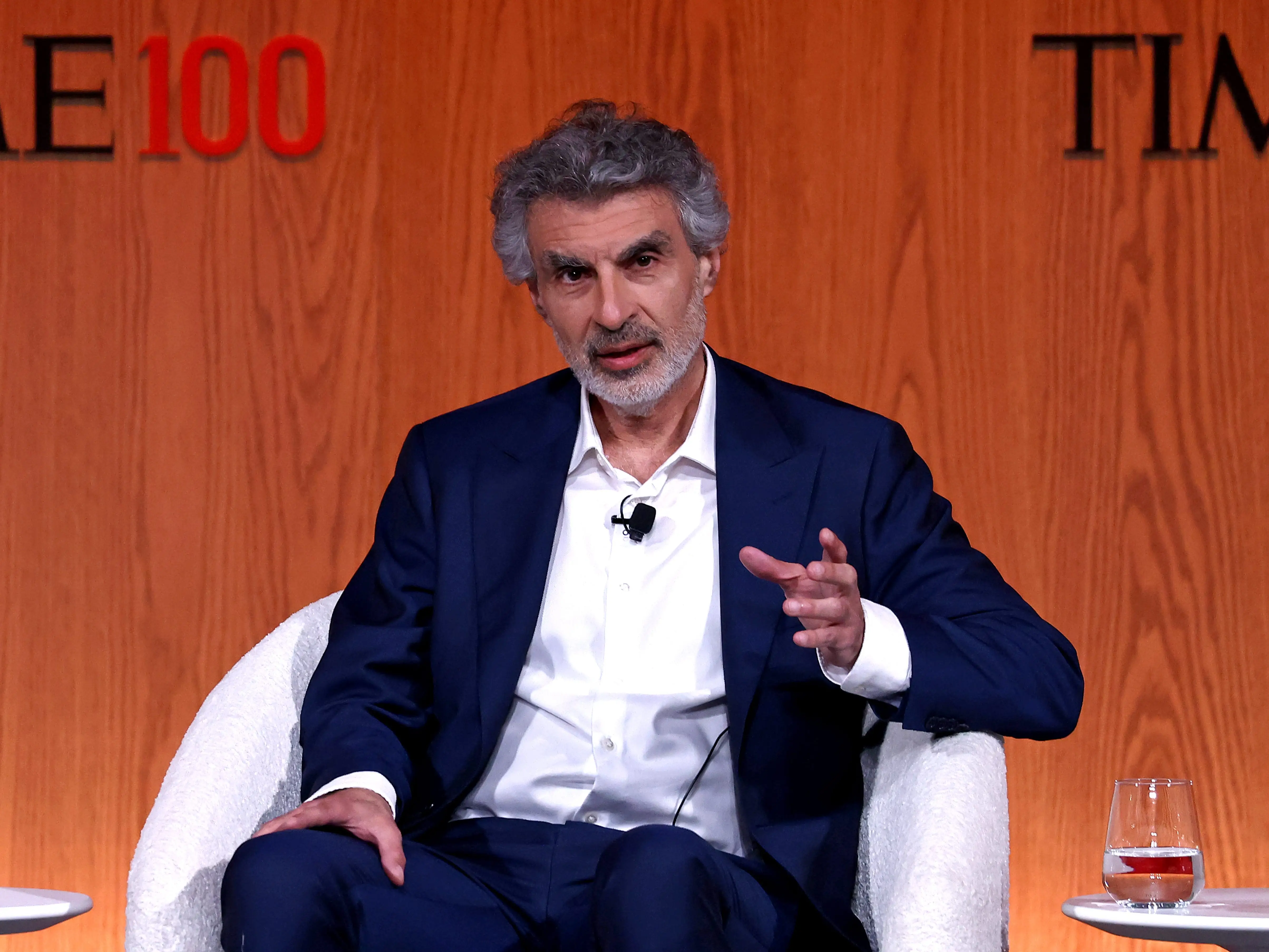 Yoshua Bengio in a blue suit sitting on a white chair.