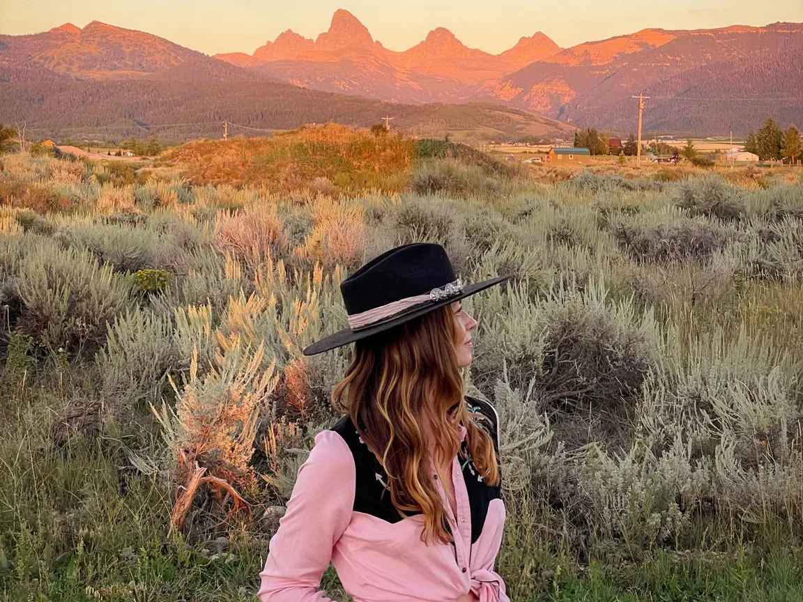 Emily stands in a field at sunset with mountains in the background.