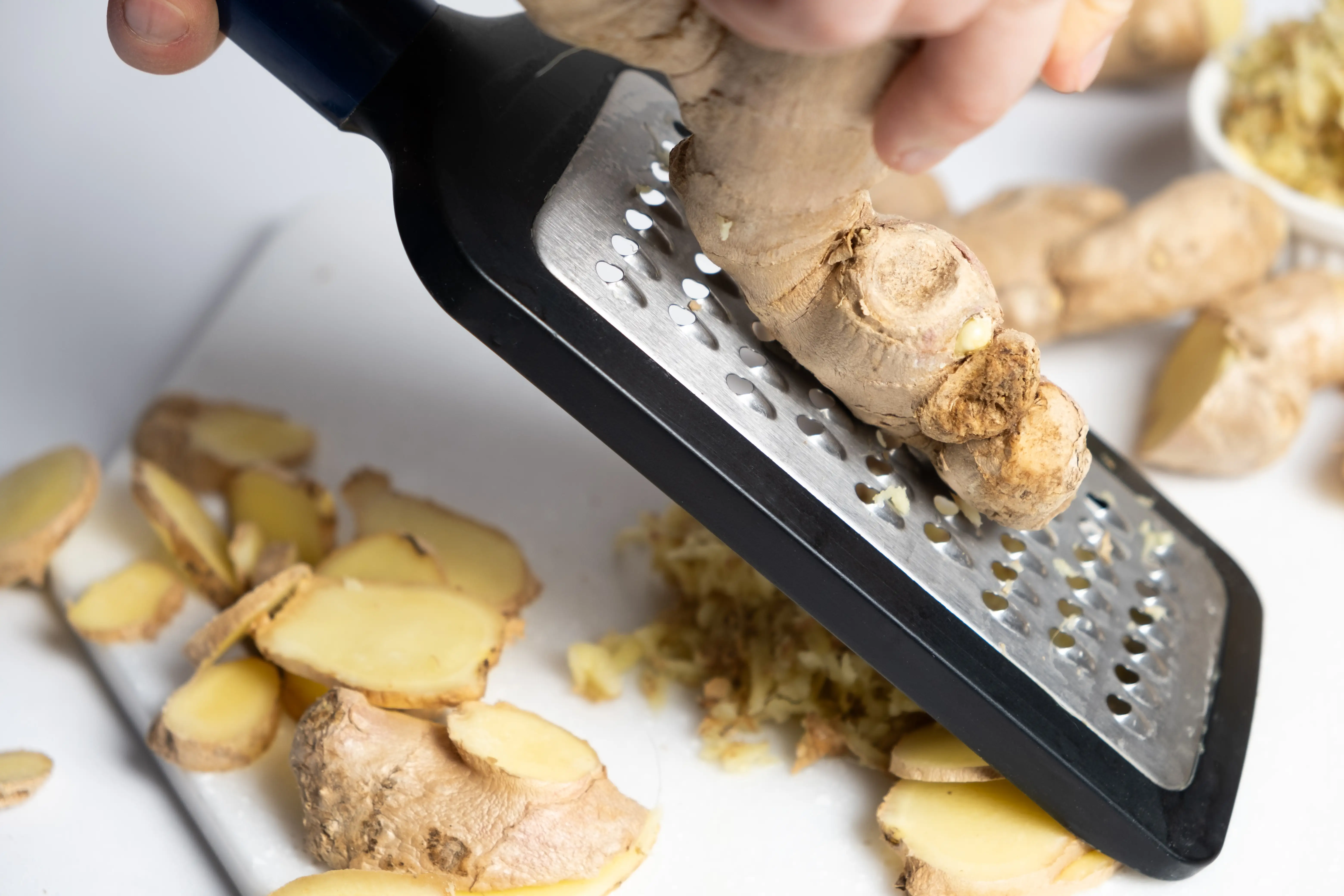 A close up of piece of sliced ginger and whole ginger being grated on a kitchen tool