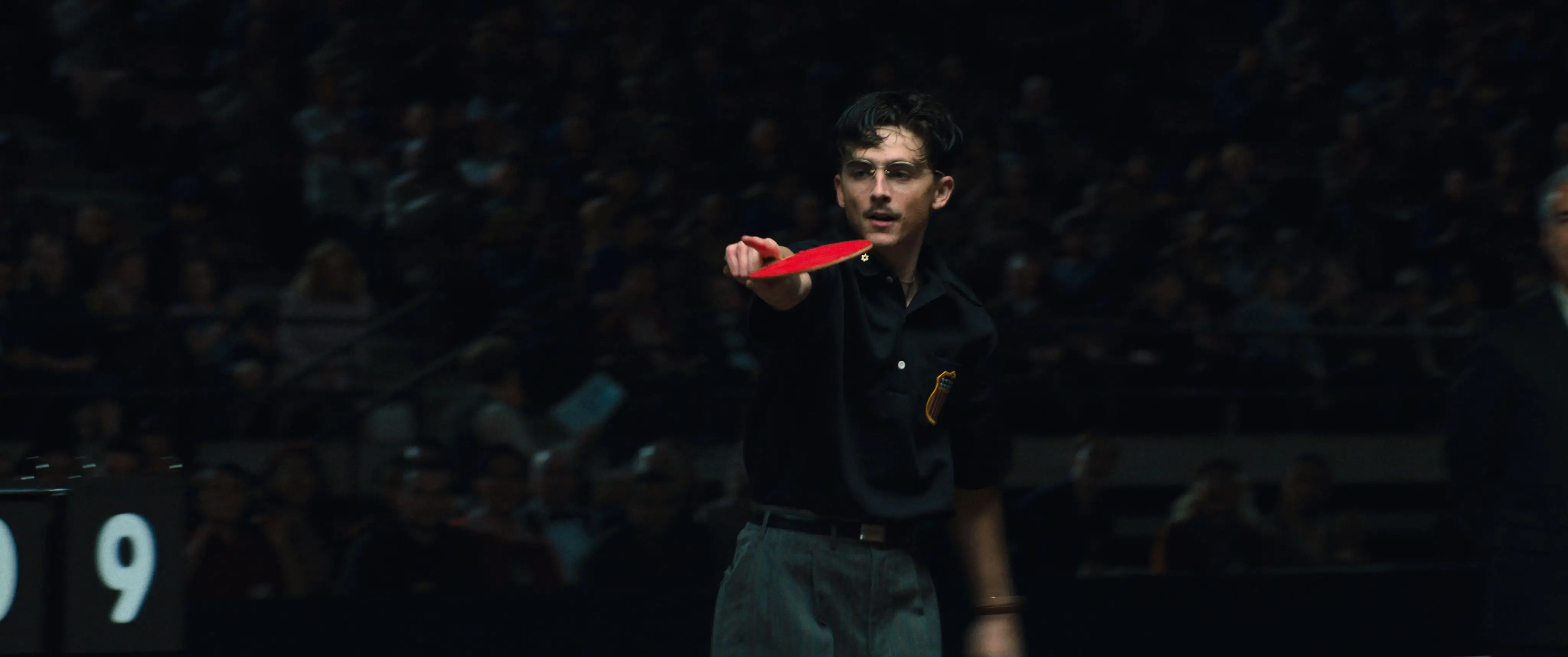 Timothée Chalamet pointing while holding a ping pong paddle in Marty Supreme