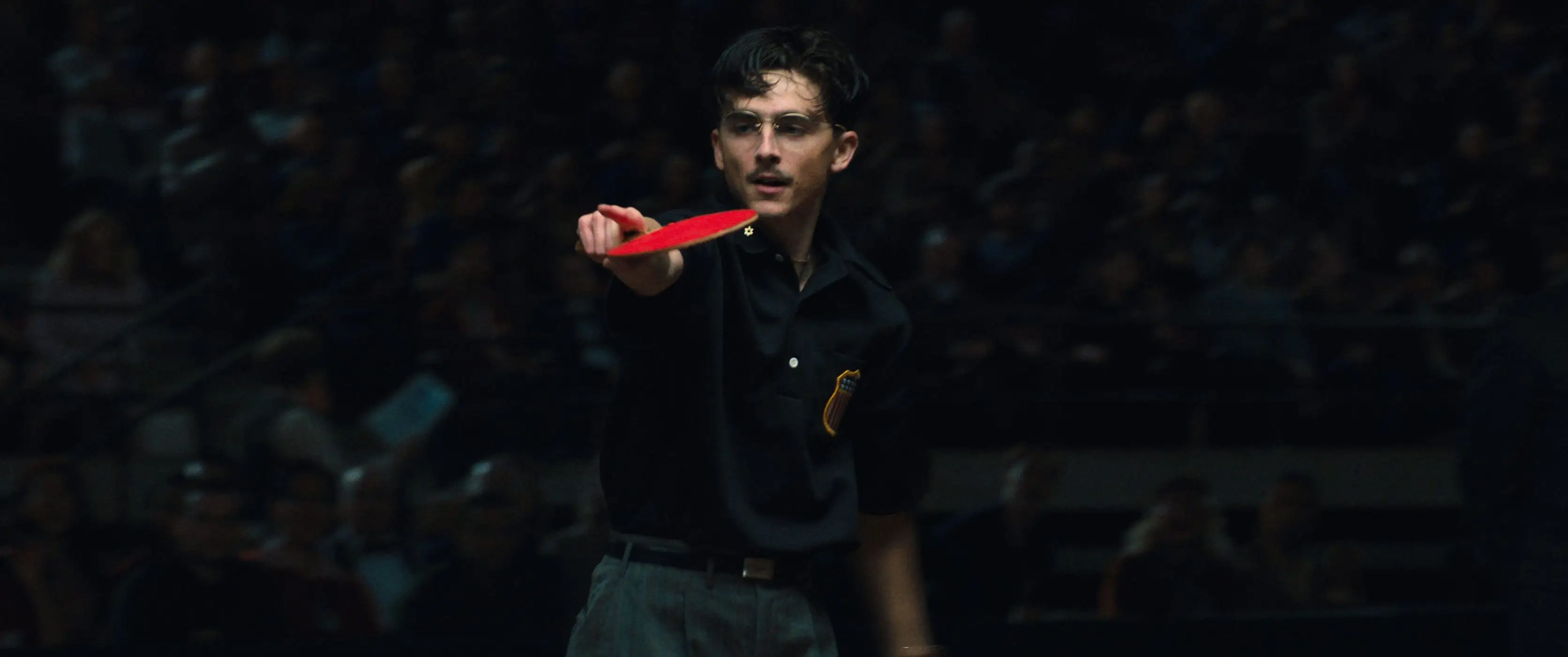 Timothée Chalamet pointing while holding a ping pong paddle in Marty Supreme