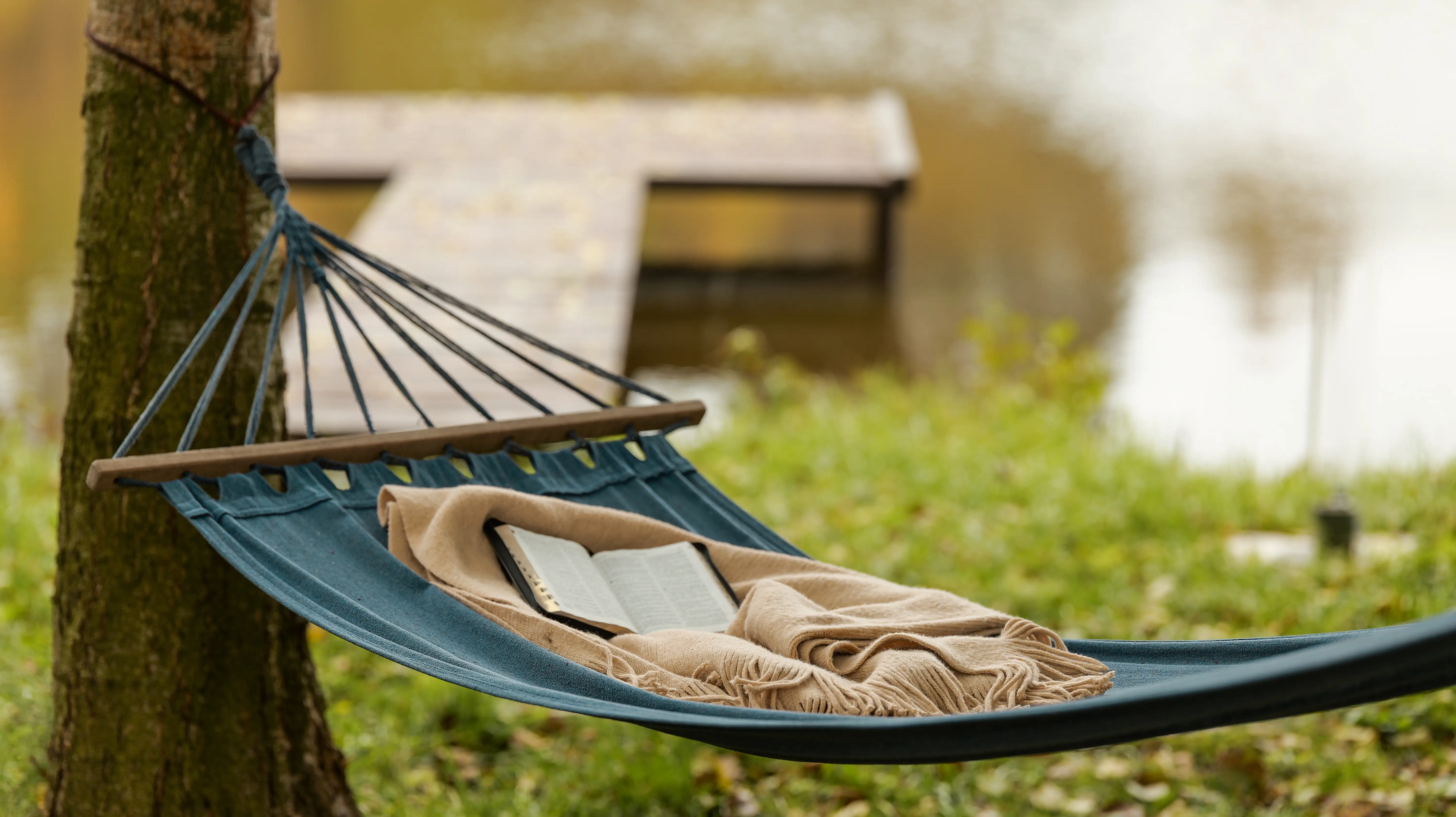 A relaxing hammock next to a pond with a book for taking a break and resting