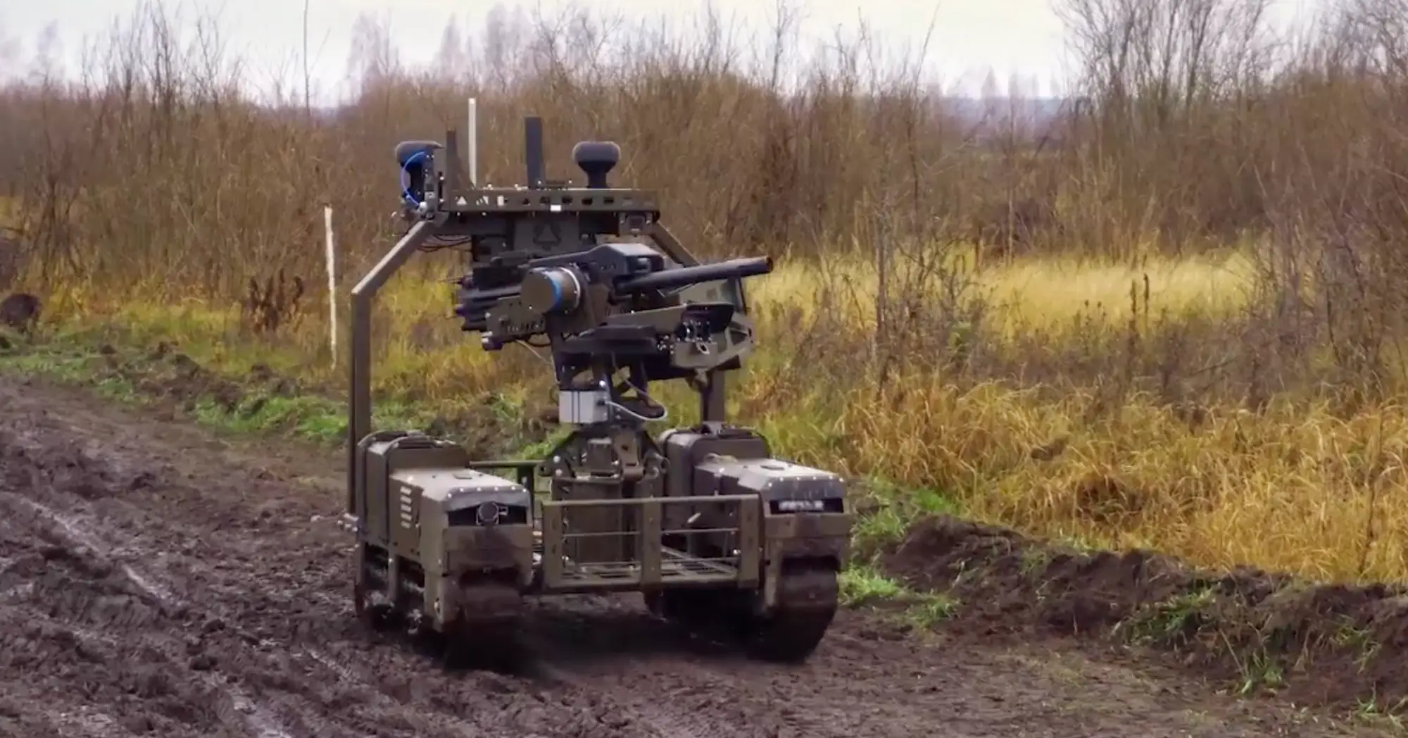 A robot on tracks driving down a muddy track with a grenade launcher on top