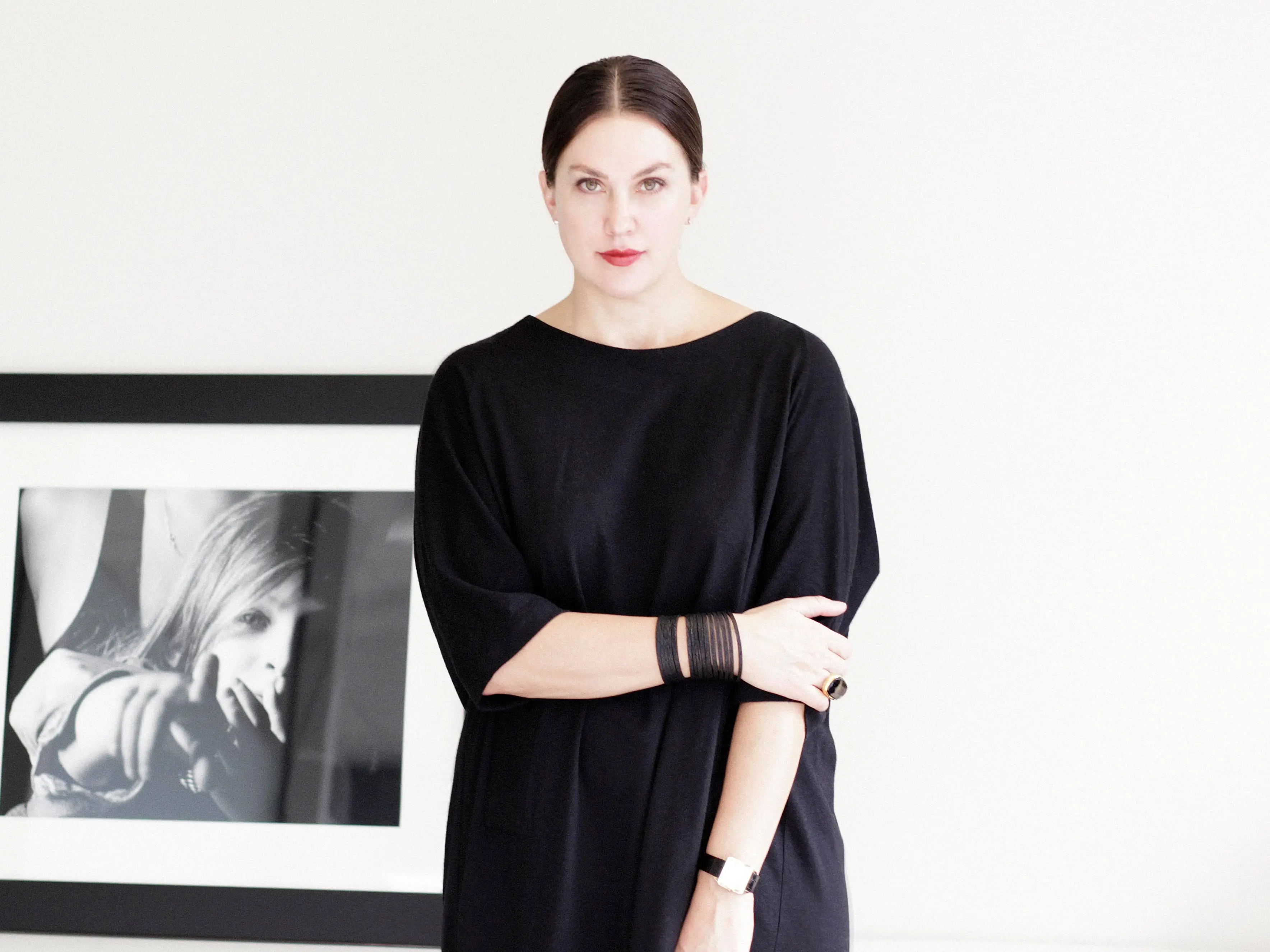 a woman in a black dress stands in front of a white wall