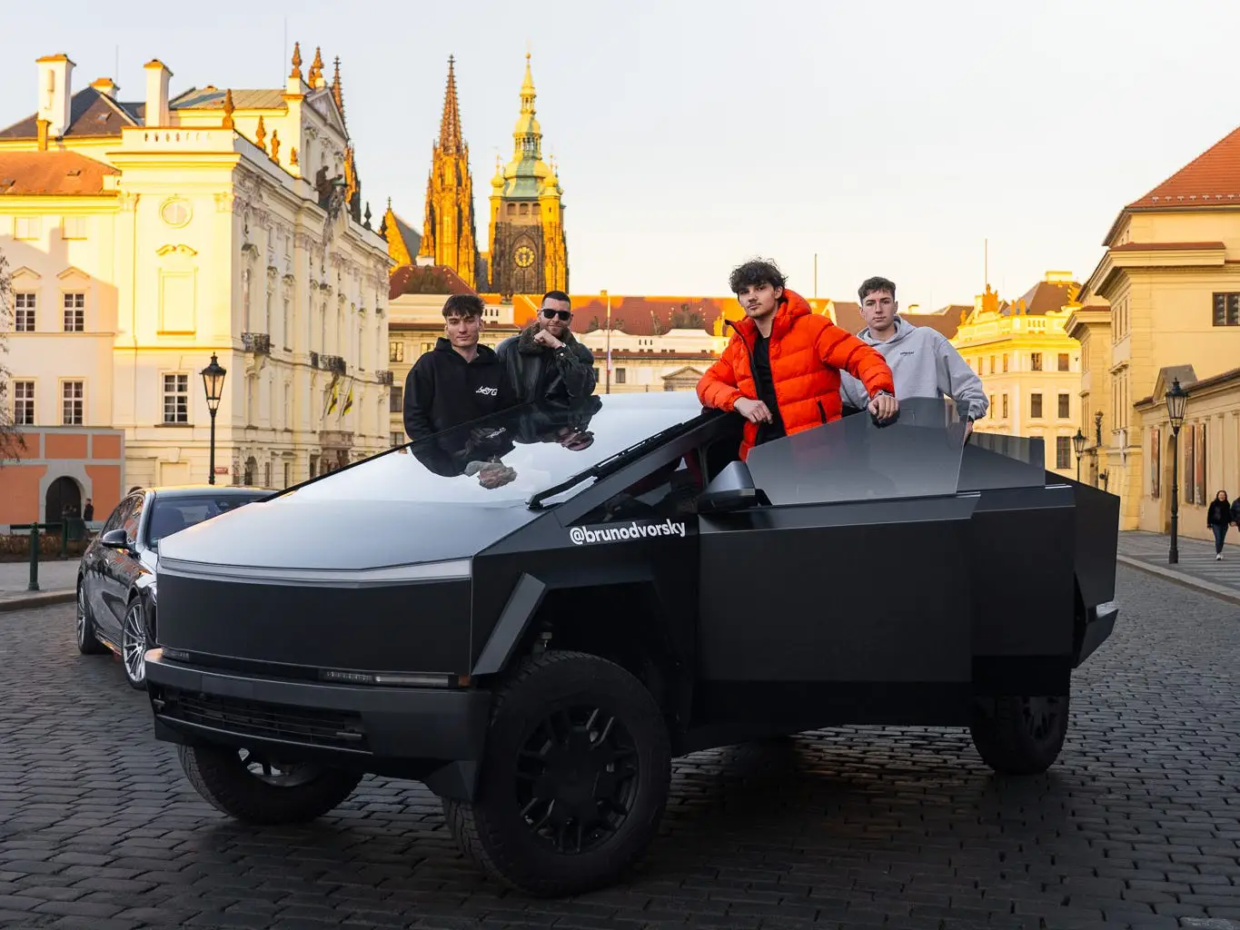 Four men pose with a Tesla Cybertruck in a medieval square in Prague.