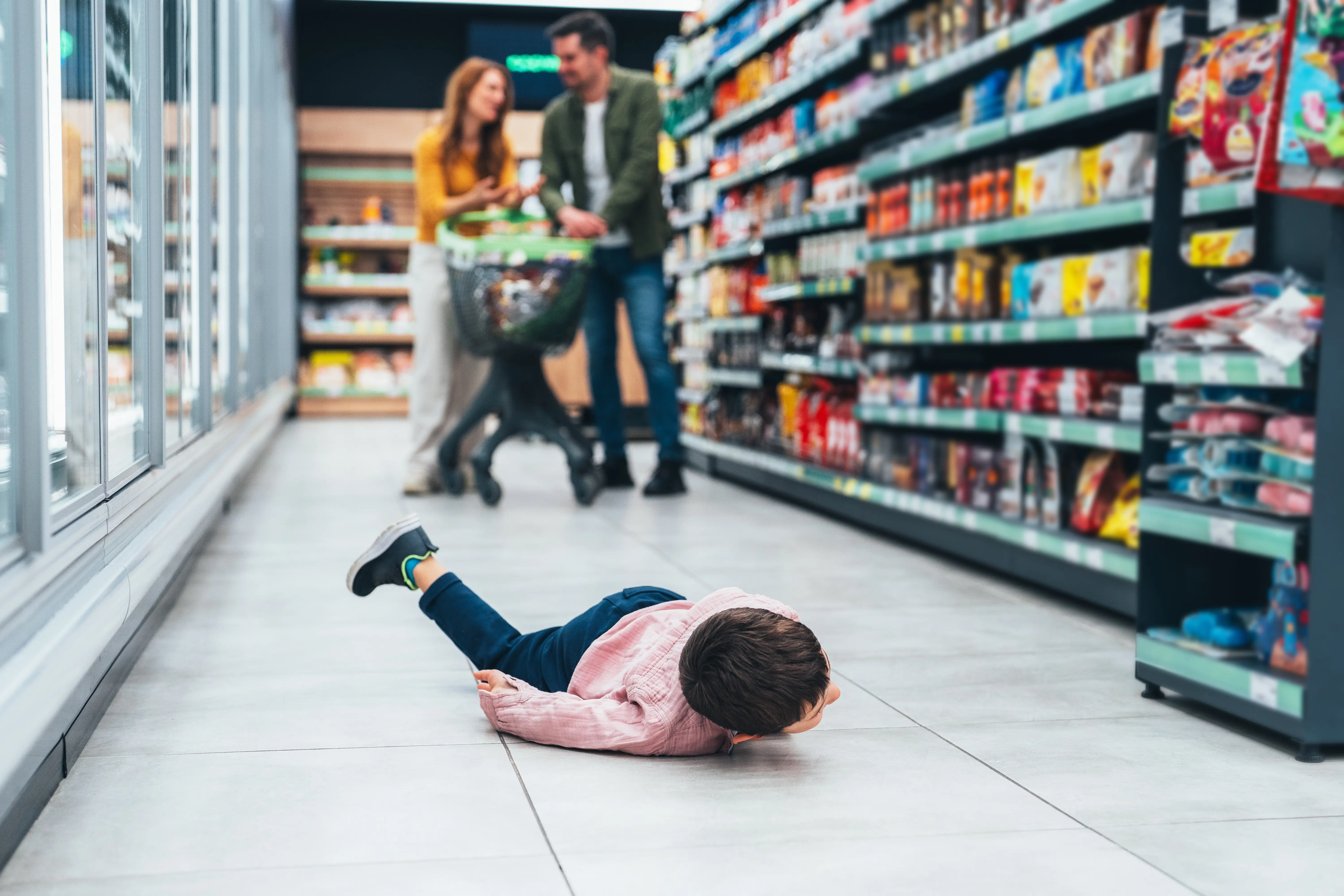 Shot of small boy lying on floor and fusses while his mom and dad shops for groceries.