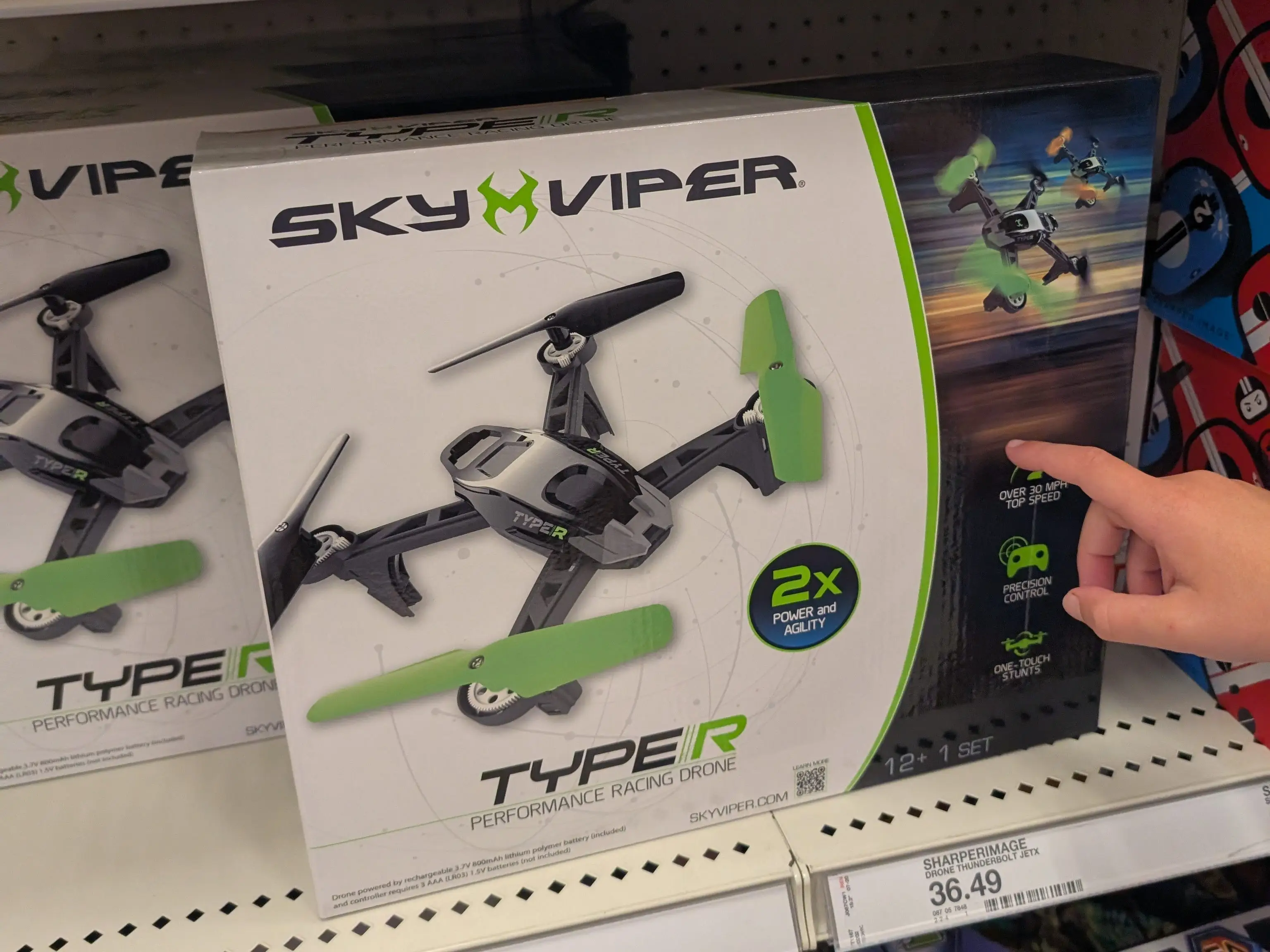 A young child points to a drone toy on a shelf in a store.