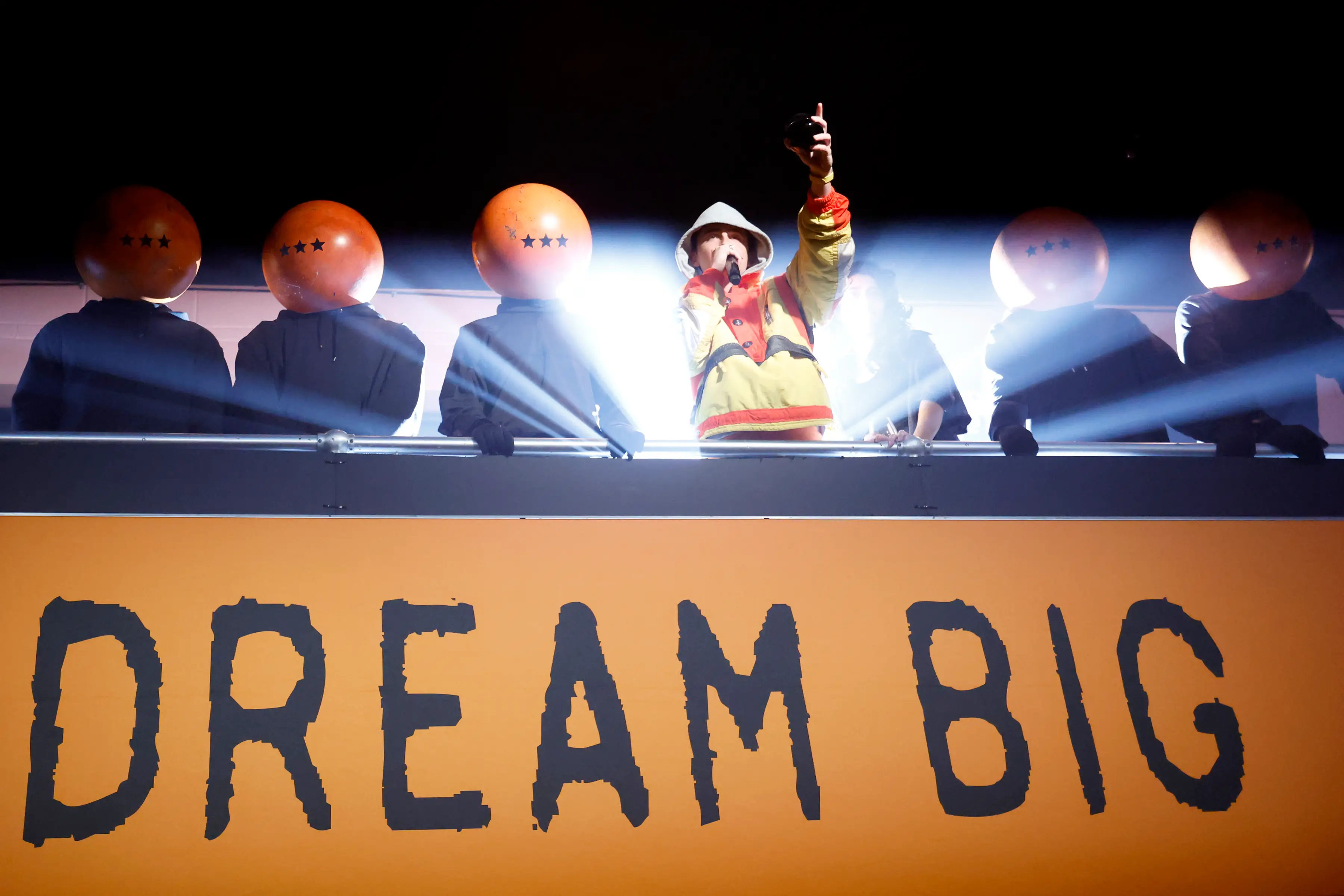 Timothee Chalamet in a hood speaking into a microphone surrounded by people in large ping pong balls