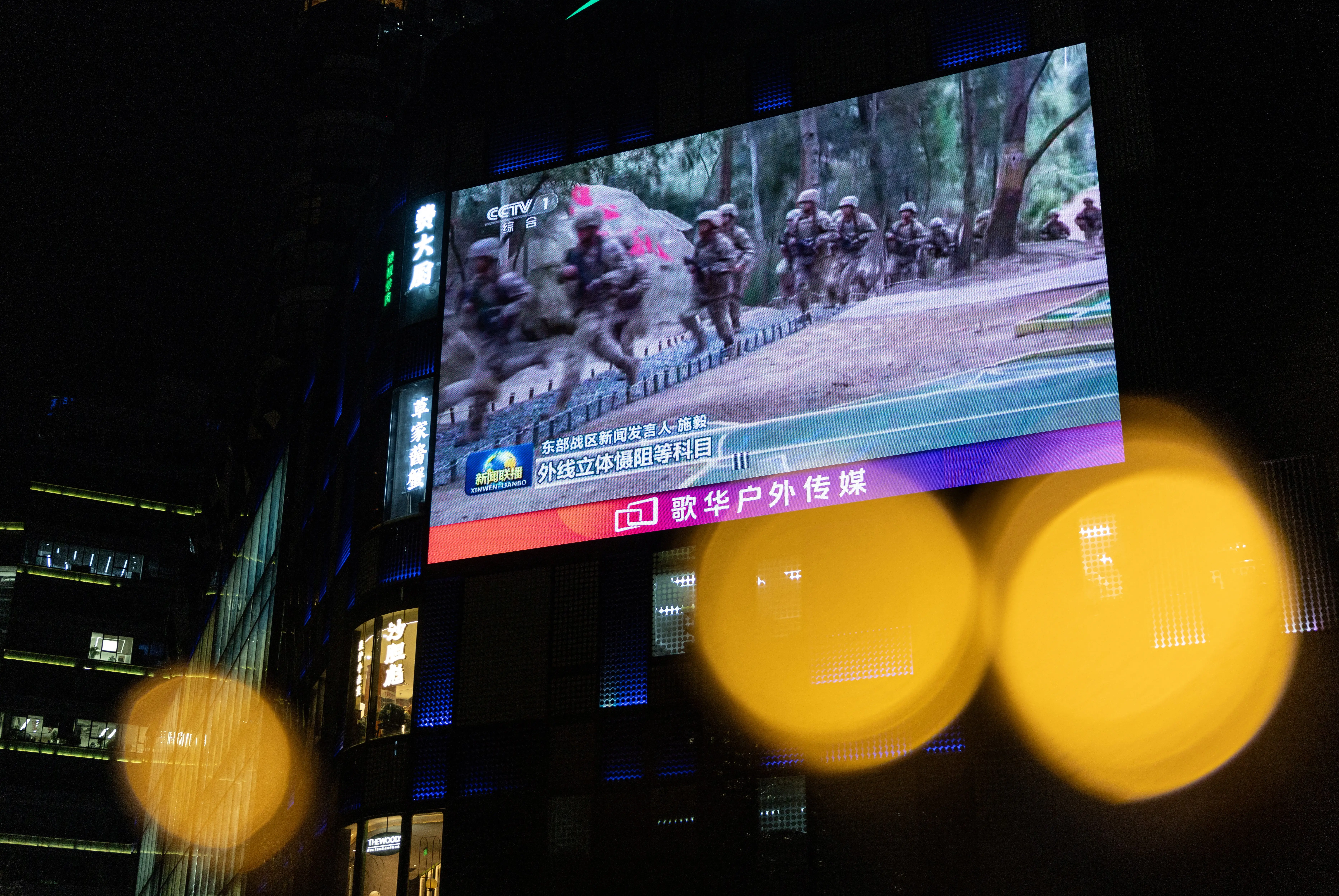 A screen showing soldiers running is seen against a building in a city.