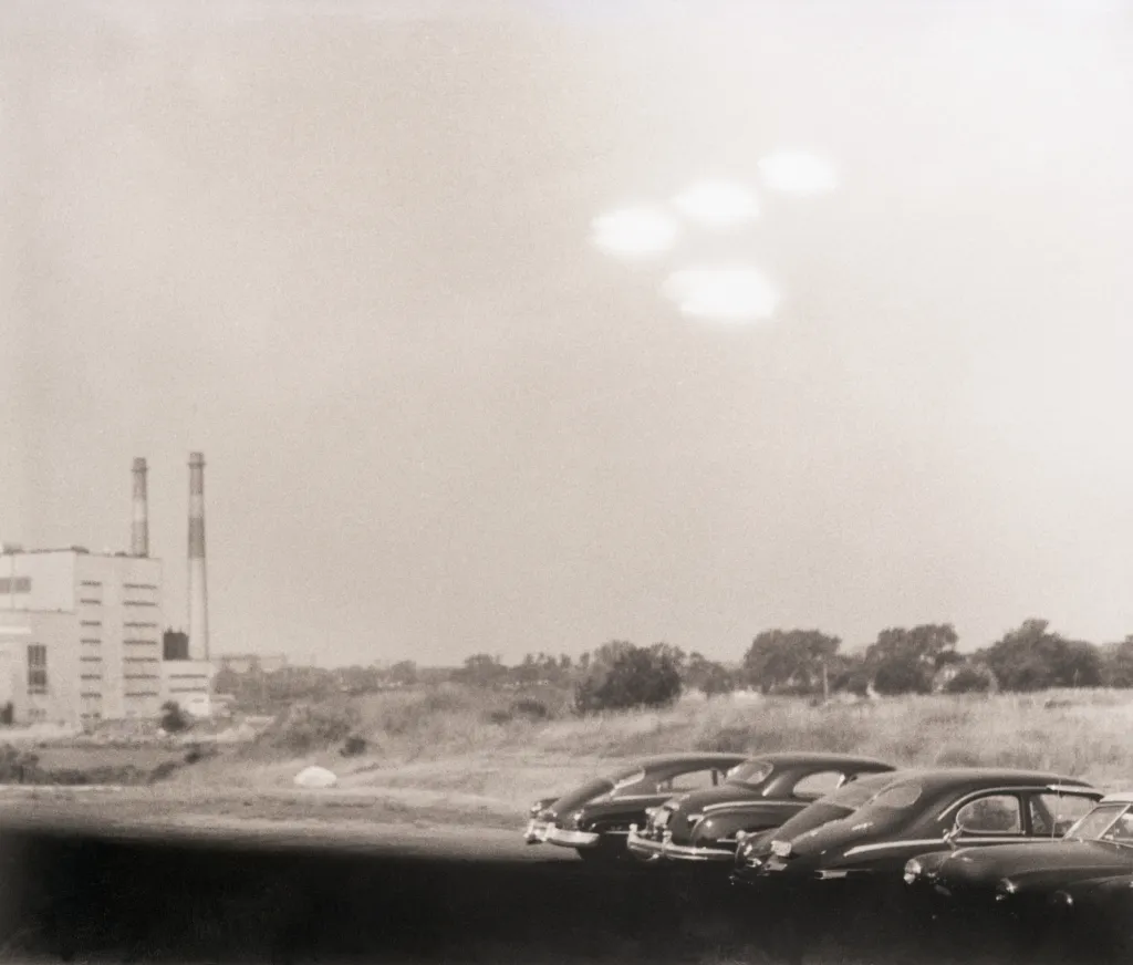 Multiple unidentified flying objects in the sky above a factory and parked cars in Salem, MA.