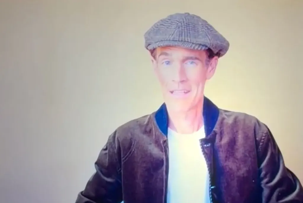 James Van Der Beek wearing a grey flat cap and a dark jacket over a white t-shirt.