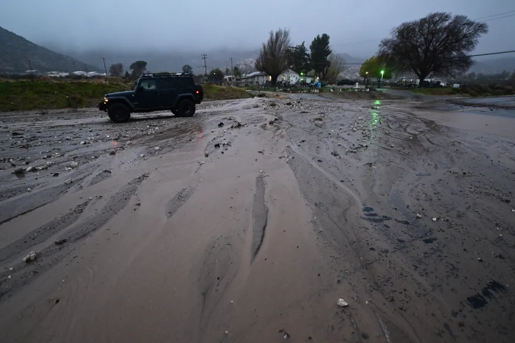 A car drives over mud along California State Route 138 after flooding Wednesday, Dec. 24, 2025, outside of Wrightwood, Calif.