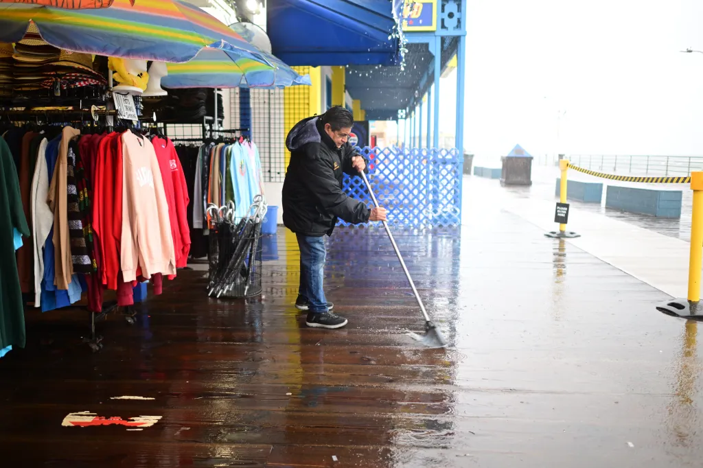 Miguel Lopez sweeps water from Marlene's Beachcomber on the Santa Monica pier Wednesday, Dec. 24, 2025