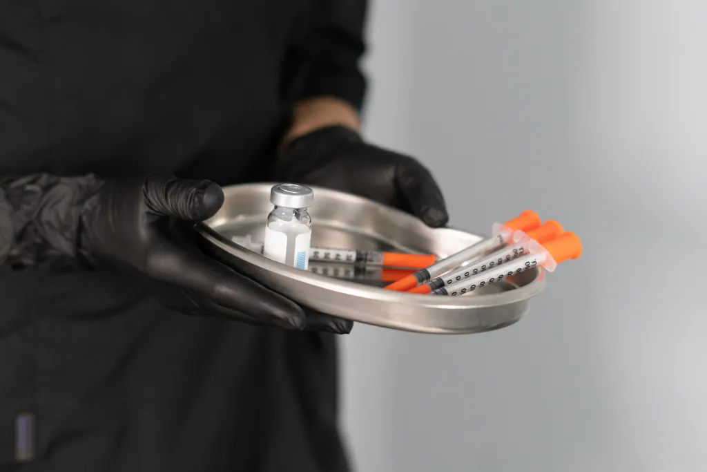 A cosmetologist's gloved hands holding a tray with multiple syringes and a vial, preparing for a botox injection.