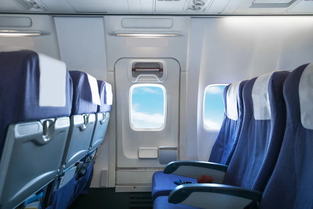 Interior of an airplane cabin with empty blue seats and windows showing a blue sky.
