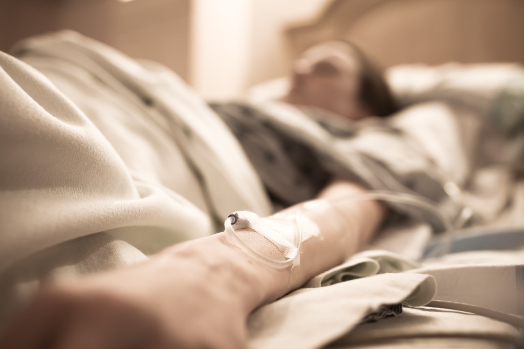 Sick woman lying in a hospital bed with an IV in her arm.