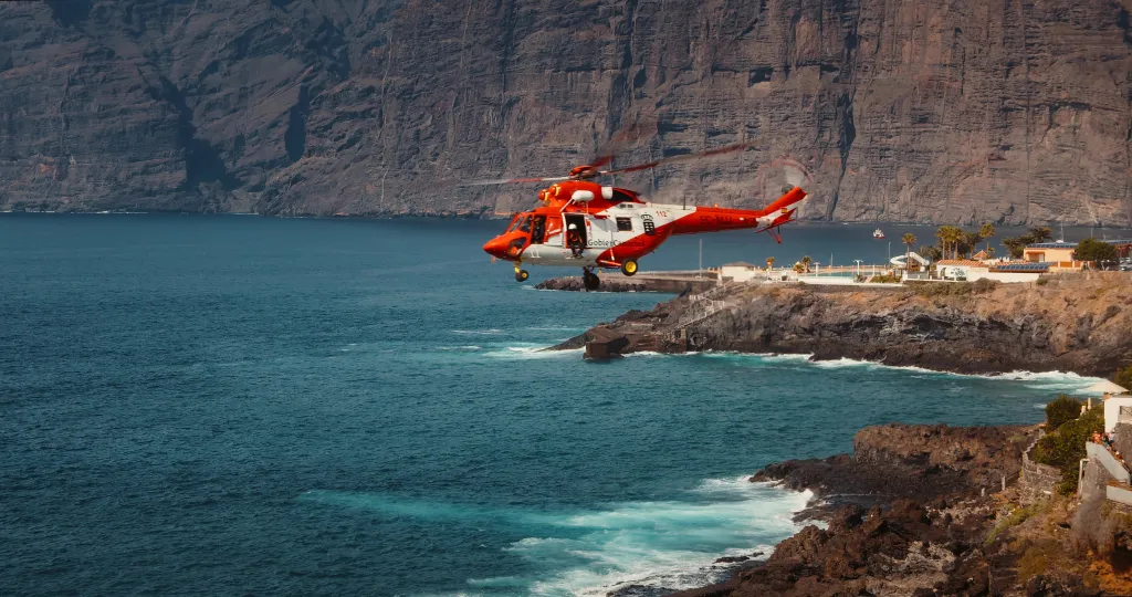 Rescue helicopter flying over a stormy ocean near rocky coastline.